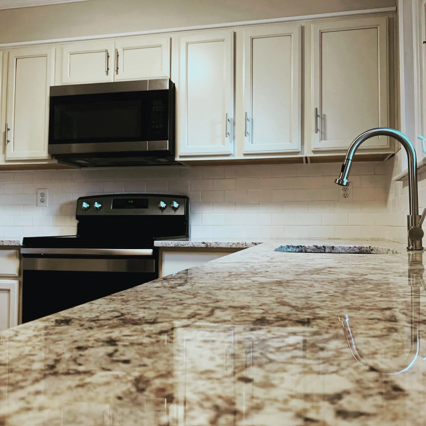 Kitchen with white cabinets, granite countertop, black stove, microwave, and stainless steel faucet.