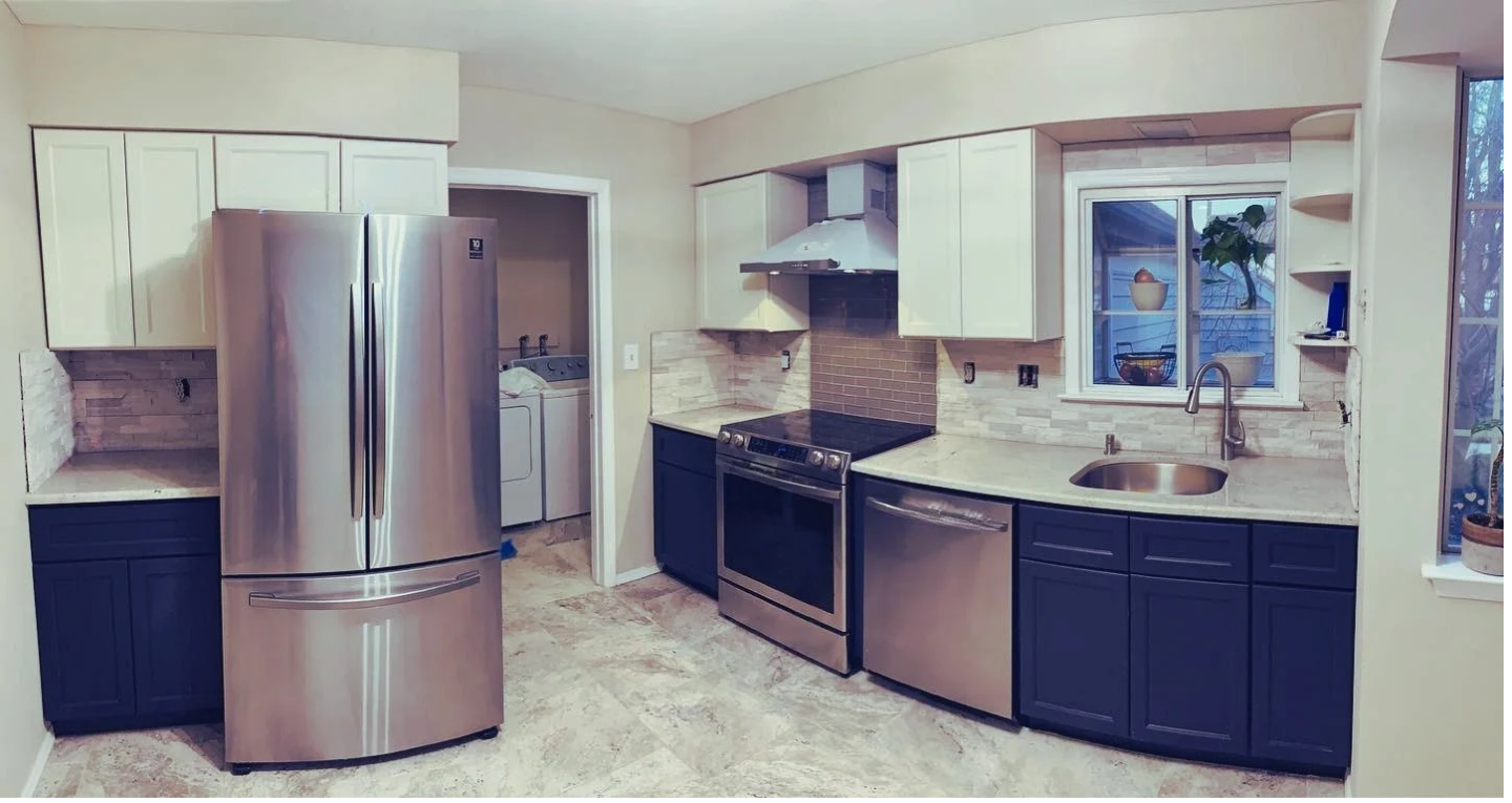 Modern kitchen with stainless steel appliances, white upper cabinets, dark lower cabinets, granite countertops, a window above the sink, and a laundry area visible through an open door.