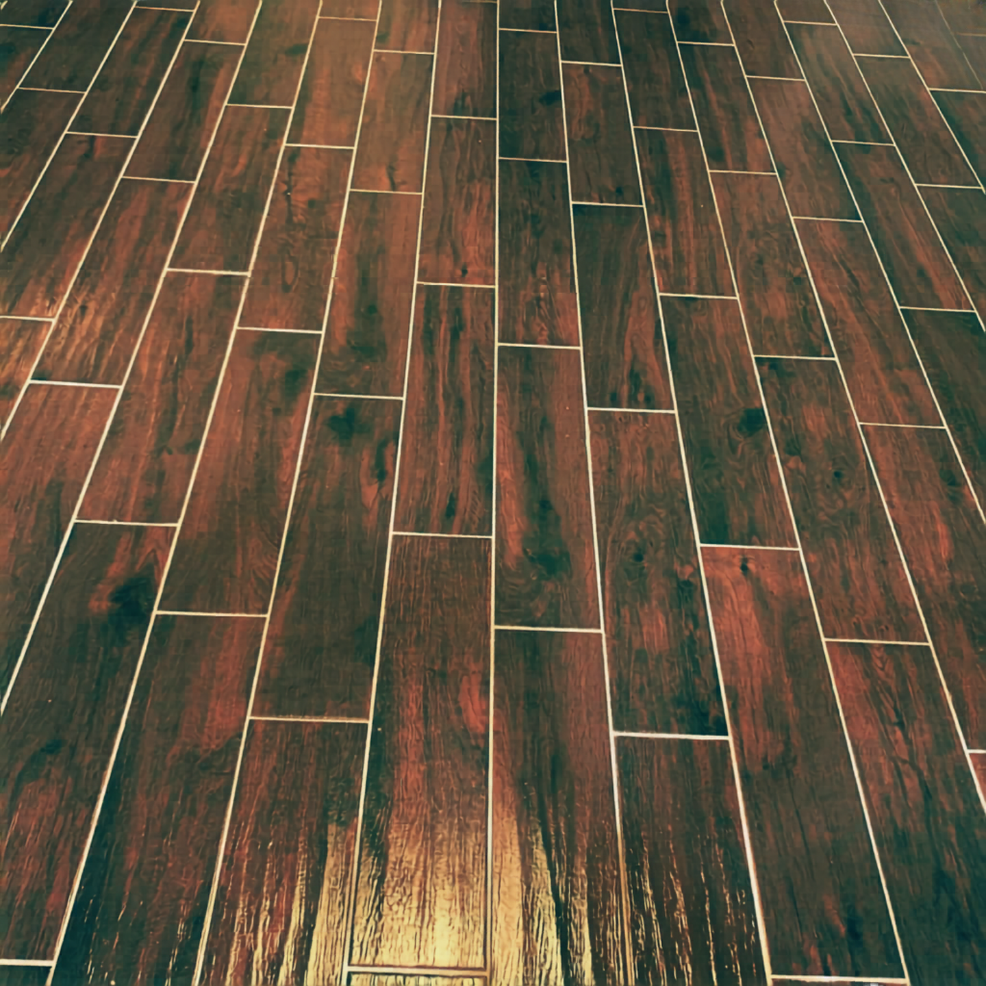 Close-up of a hardwood floor with reddish-brown color and visible wood grain, arranged in a staggered pattern.