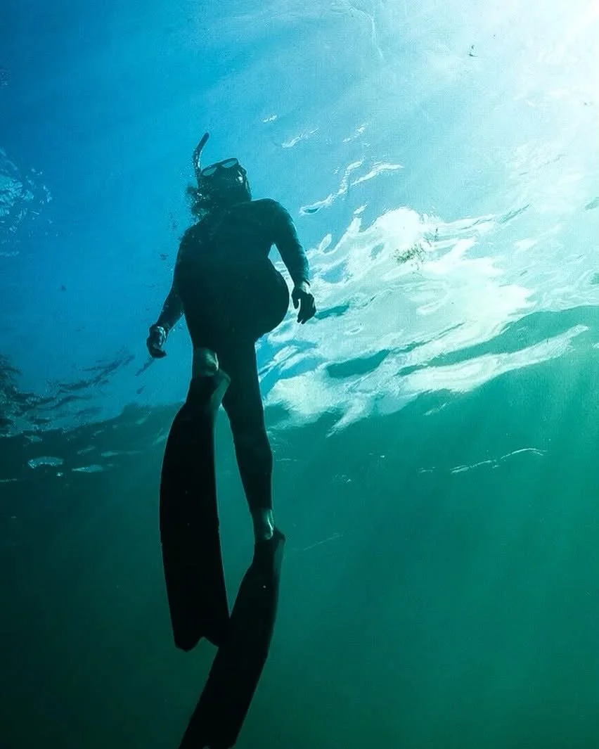 A person in scuba gear freediving underwater, floating near the surface, with a snorkel and fins.