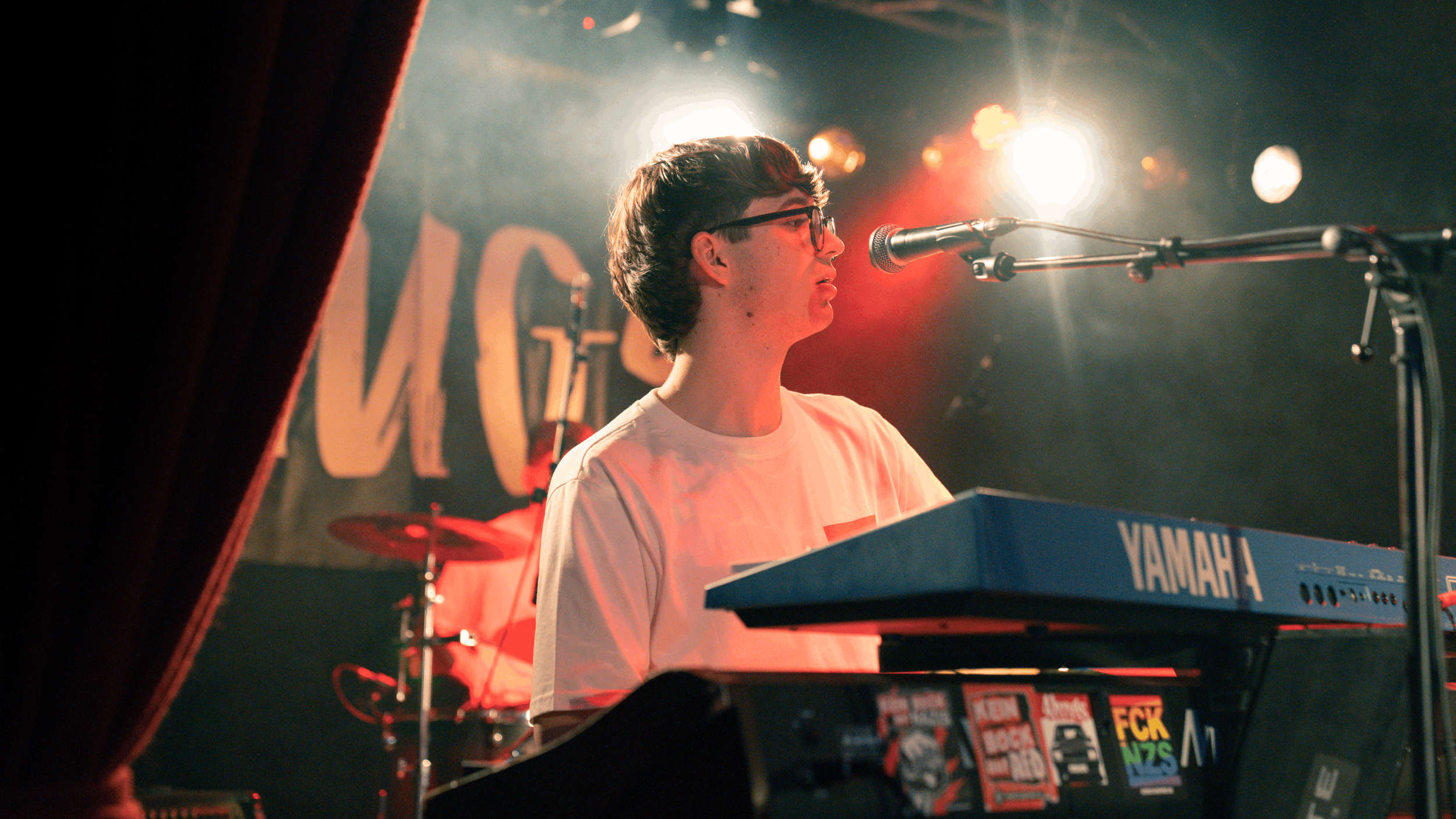 Ein junger Mann spielt Klavier auf einer Bühne, im Hintergrund sind Licht- und Bühneneffekte sichtbar.