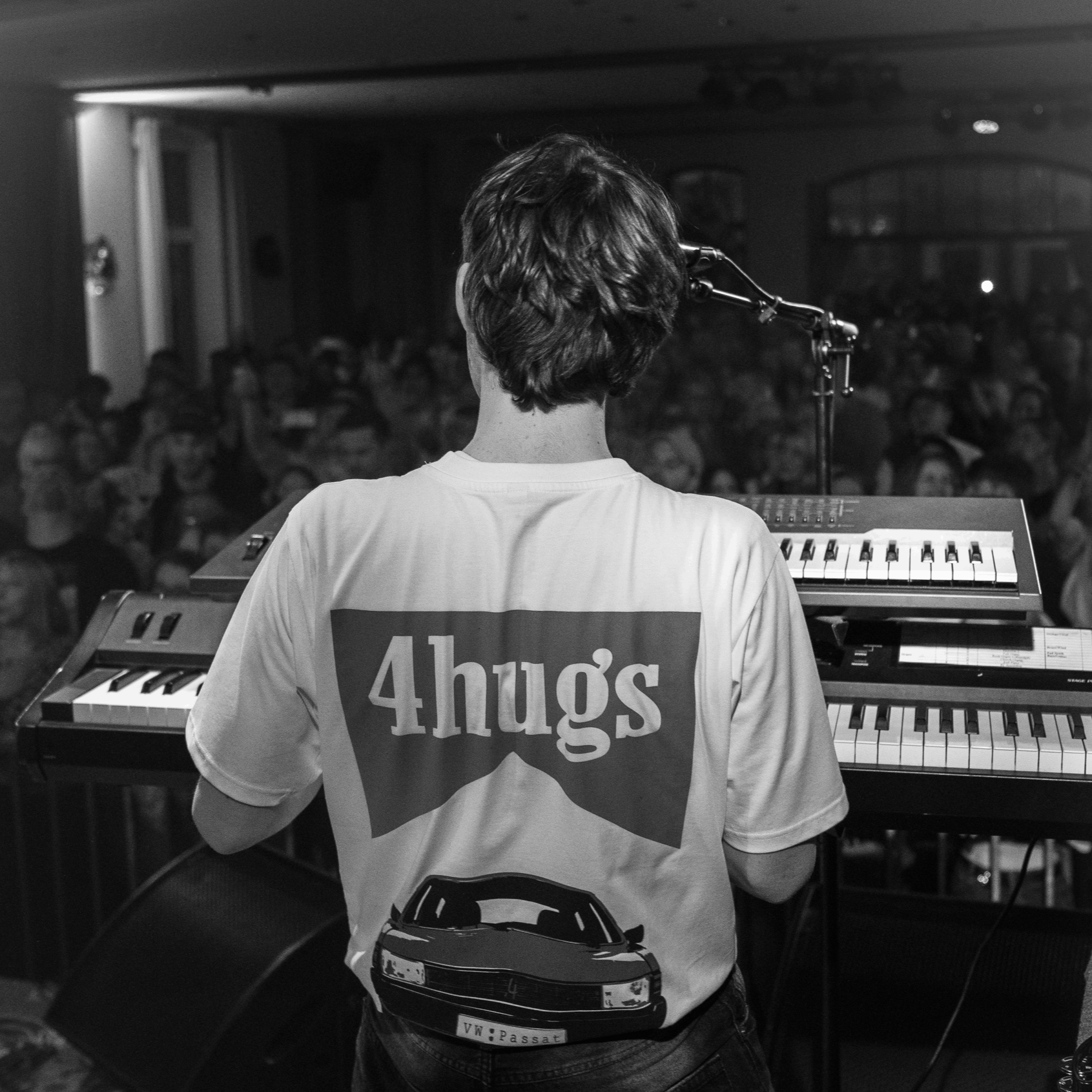 Musiker hinter einem Keyboard bei einem Live-Auftritt vor Publikum, aufgenommen von hinten, schwarz-weiß.