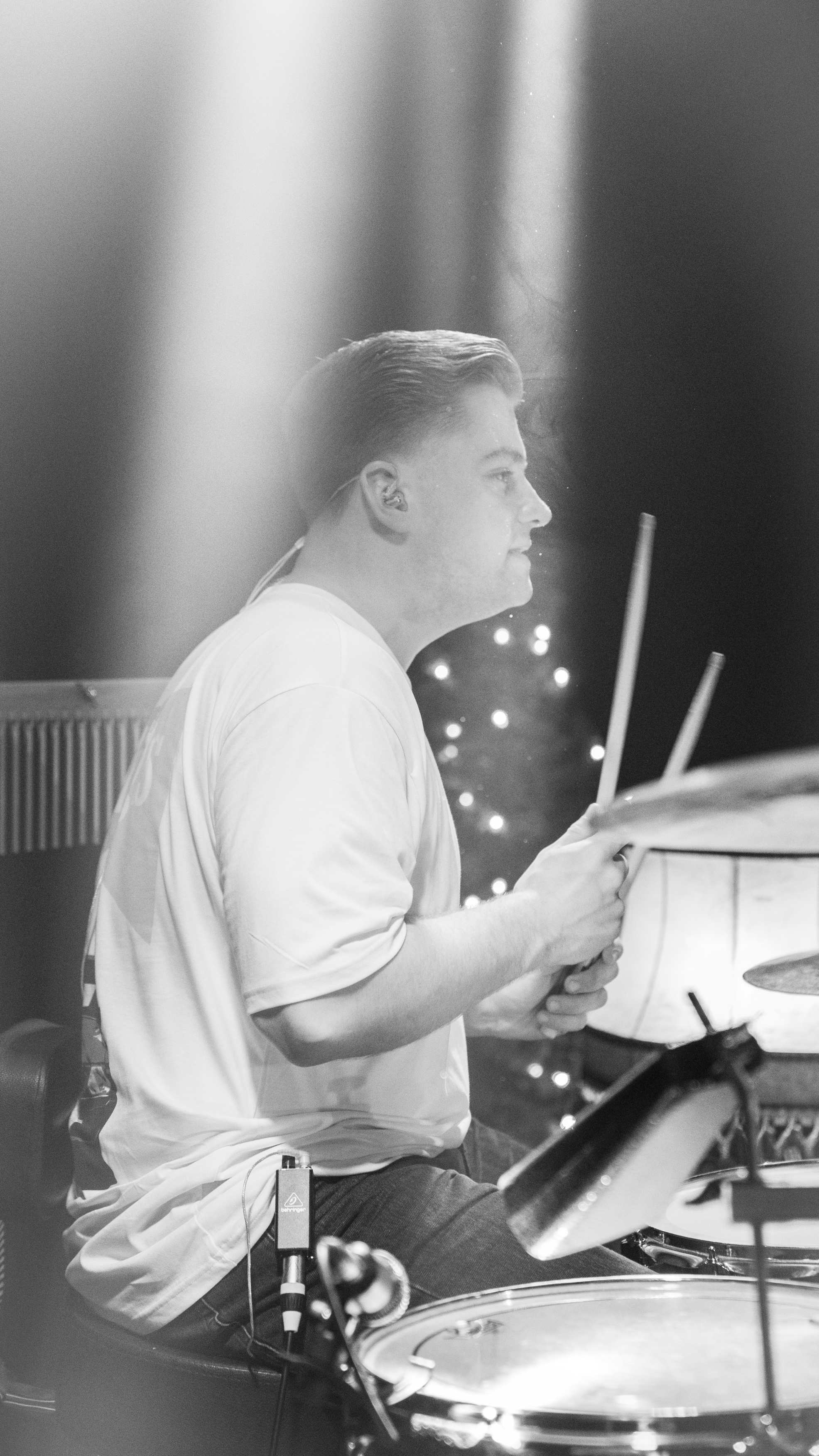 Ein Mann spielt Schlagzeug in einem dunklen Raum, beleuchtet von kleinen Lichtern, in Schwarz-Weiß.