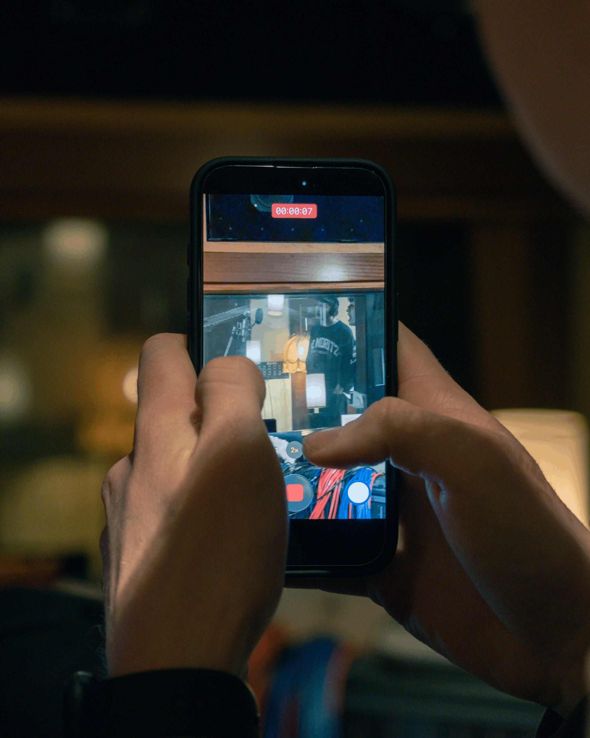 Nahaufnahme einer Person, die ein Smartphone hält und einen Kurzfilm aufnimmt, im Hintergrund unscharfe Möbel und Beleuchtung in einem Raum.
