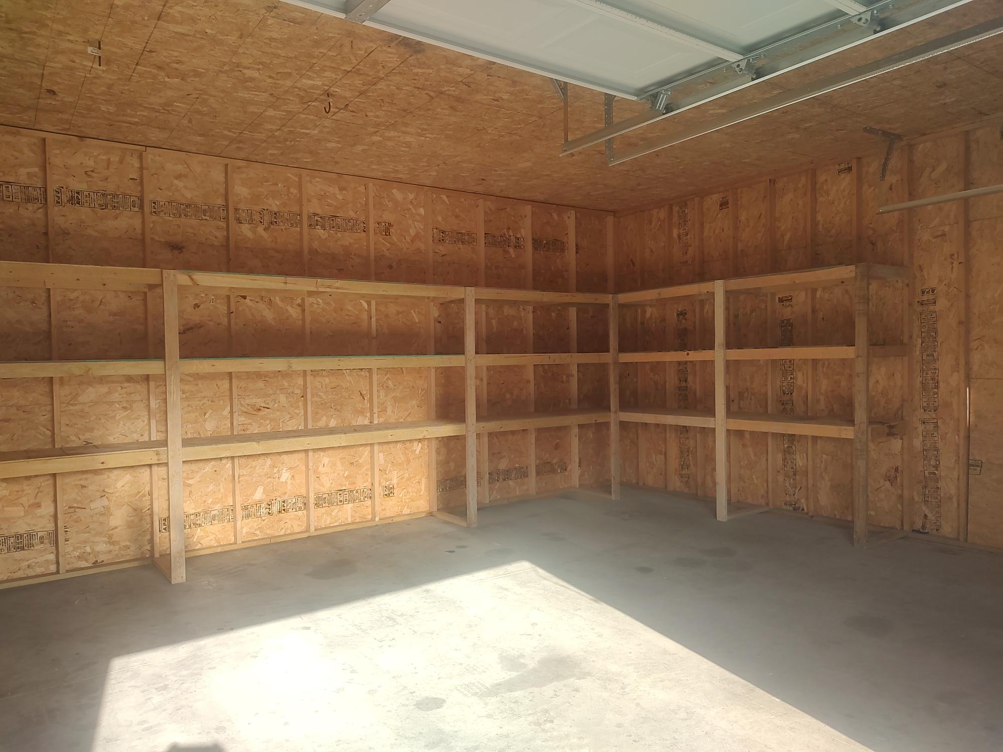 Empty garage with wooden shelves along the walls and exposed plywood panels.