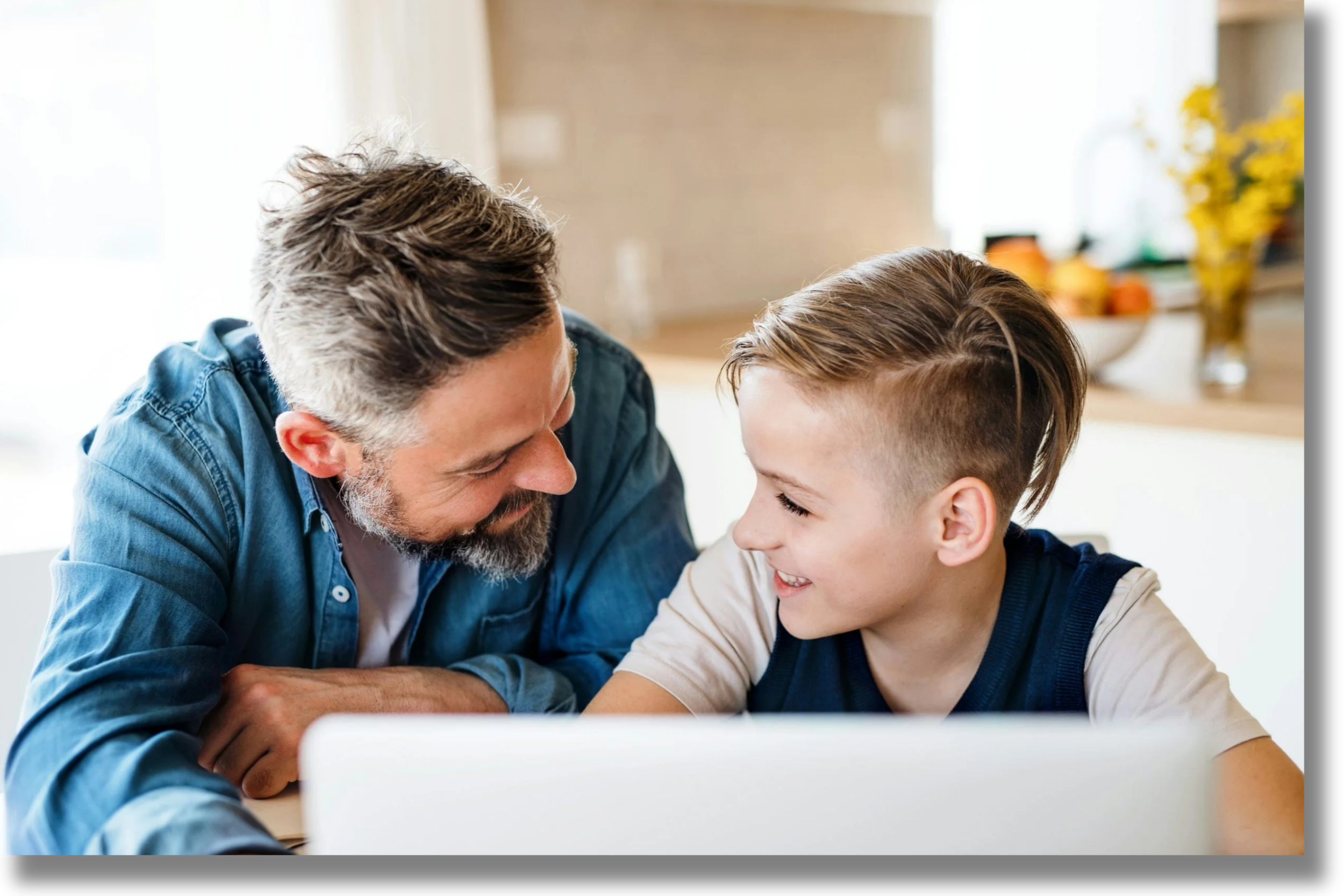 Father helping his son work on a laptop at home, representing supportive parent coaching and skill development for school-age children.