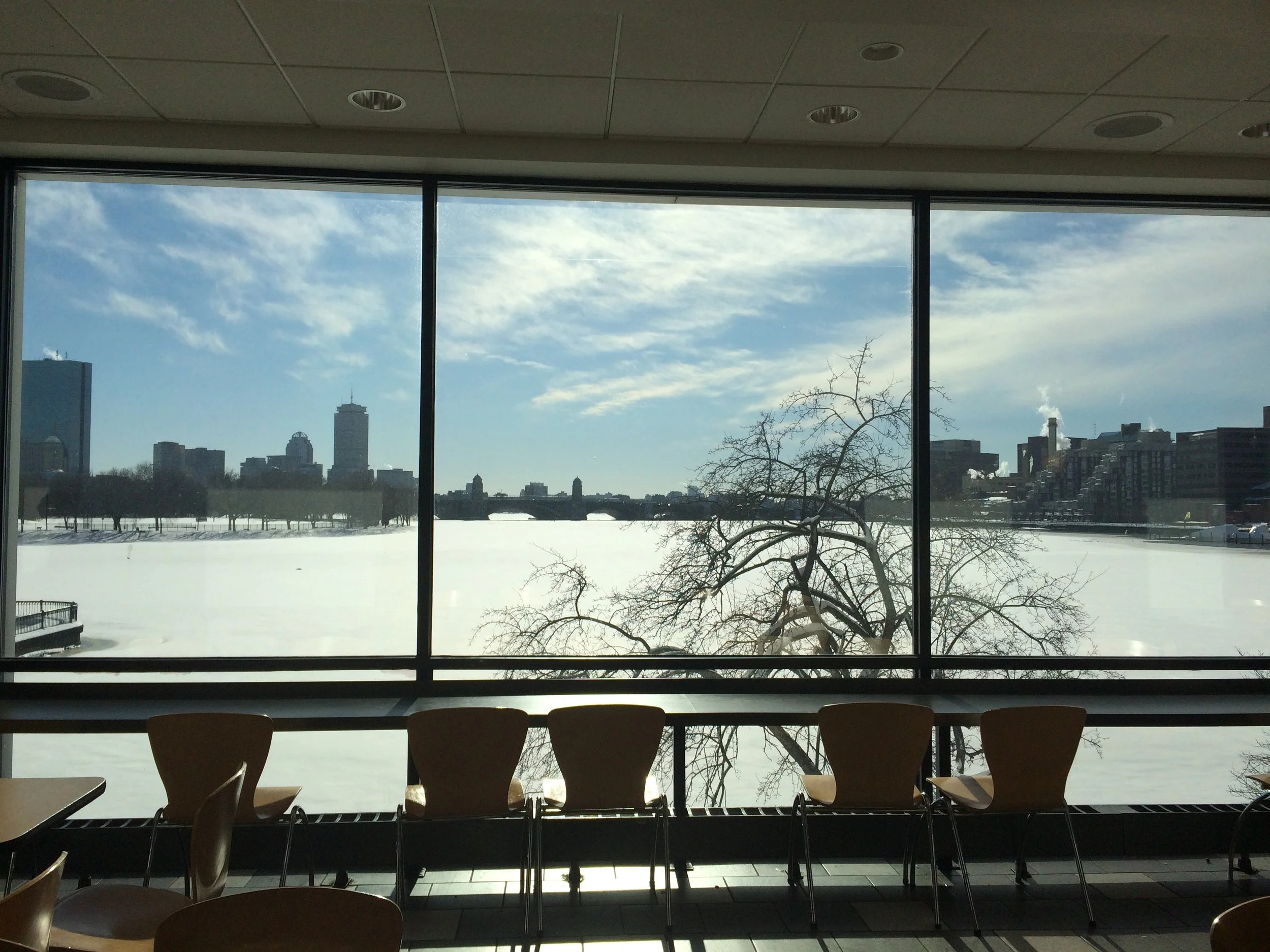 Indoor scene with chairs facing large window showing a snow-covered landscape, city skyline, and cloudy sky outside.