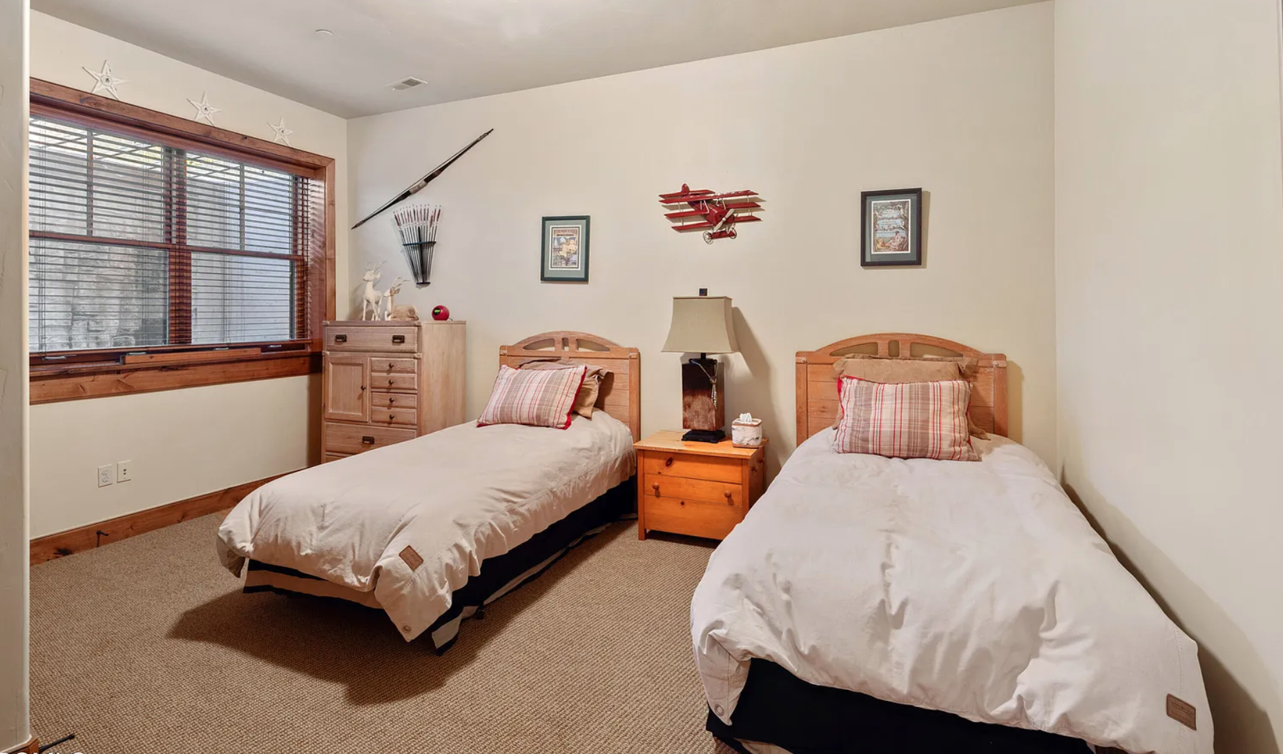 Bedroom with two twin beds, plaid pillows, wooden furniture, and airplane decor on wall.