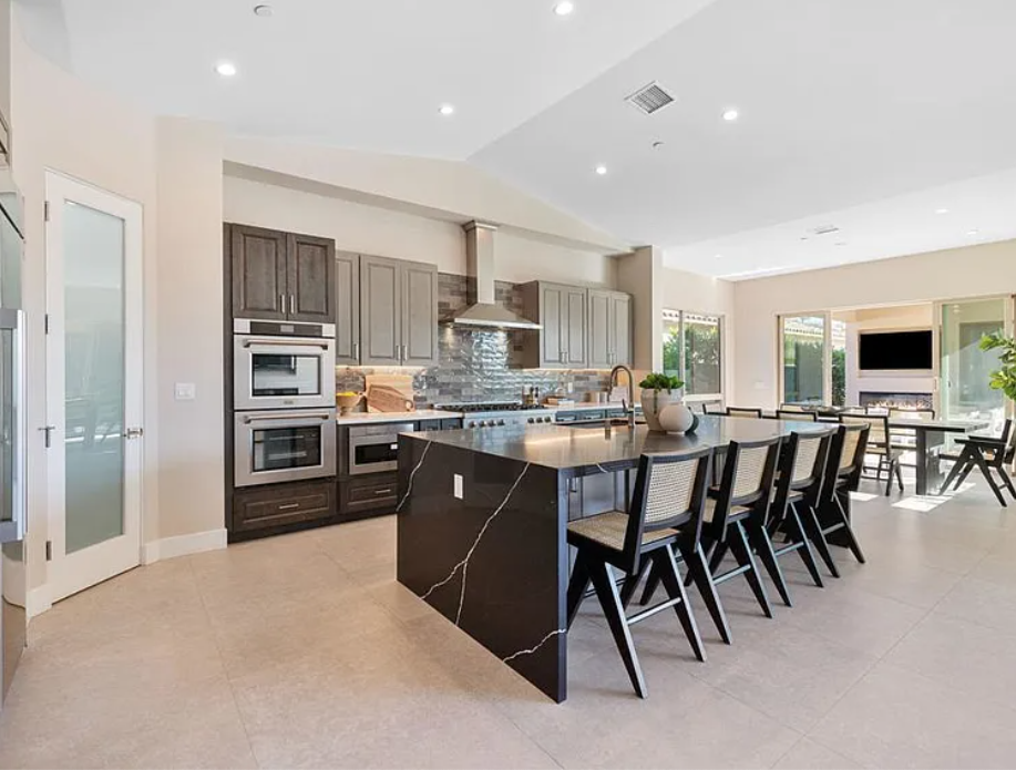 Modern kitchen with dark countertops, island seating, stainless steel appliances, light-colored cabinets, and a dining area.