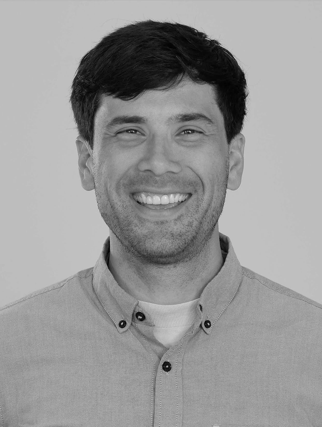 Black and white portrait of a smiling man with dark hair, wearing a collared shirt.