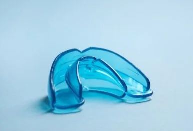 A pair of blue dental night guards placed on a light blue surface.