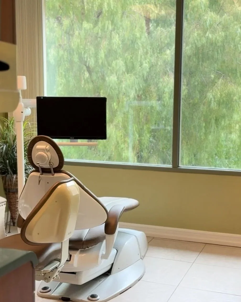 Dental or medical examination room, with modern dental chair, screen for patients, lots of greenery, large window with green trees outside.