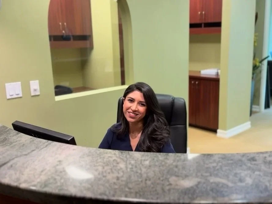 A smiling female receptionist who is on the computing and answering phone calls