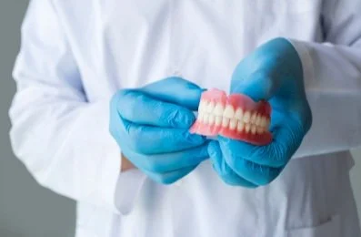 Dentist wearing gloves holding a set of artificial teeth.
