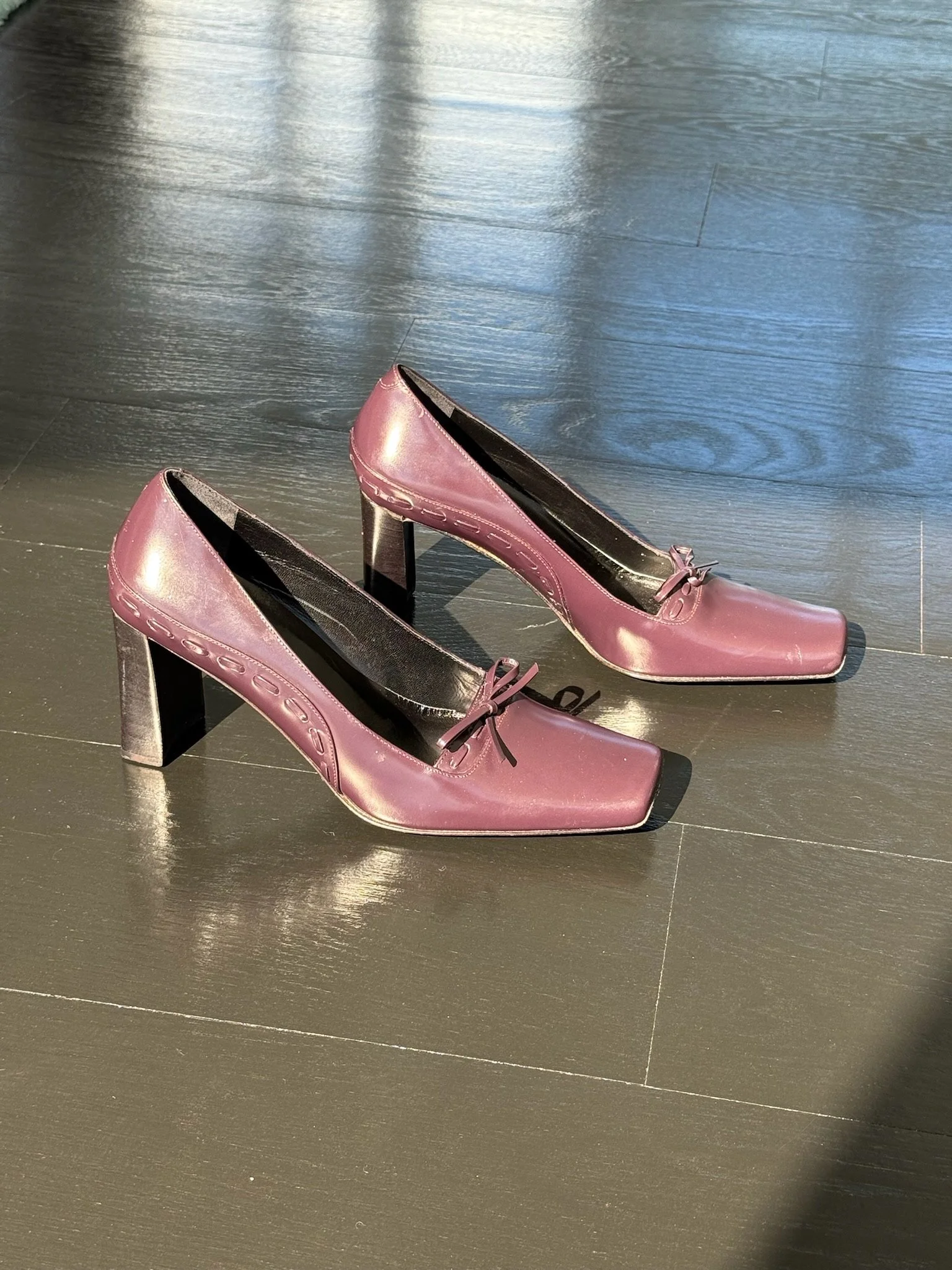 Pair of pink high-heeled shoes with bows on the top, placed on a dark wood floor.