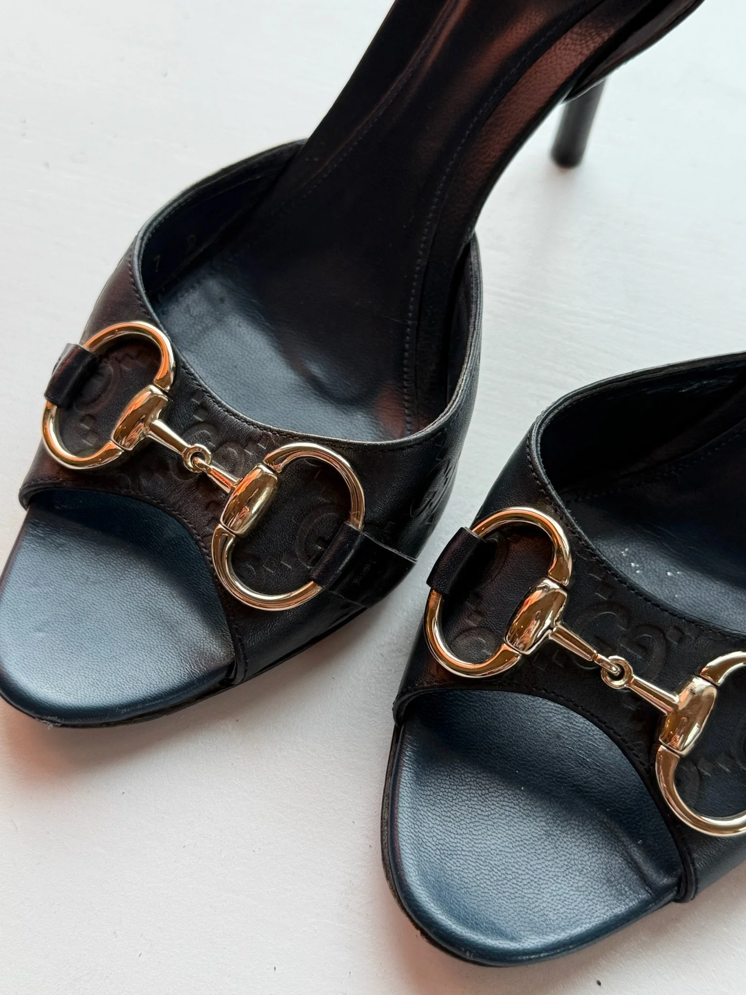 Black high-heeled sandals with gold horsebit detail at the front.