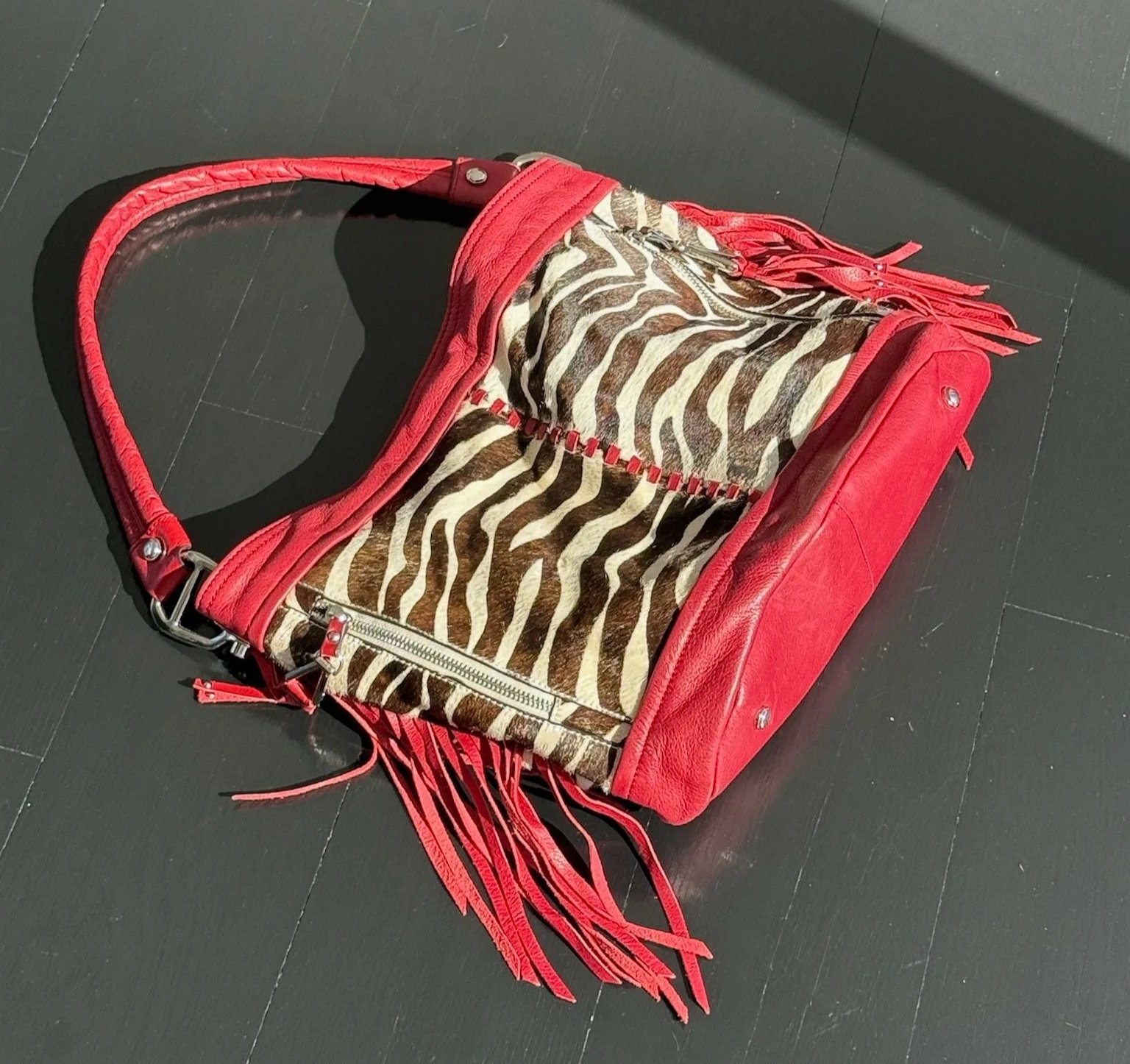 A handbag with a red leather frame and strap, featuring a zebra print fabric interior with fringe detailing.
