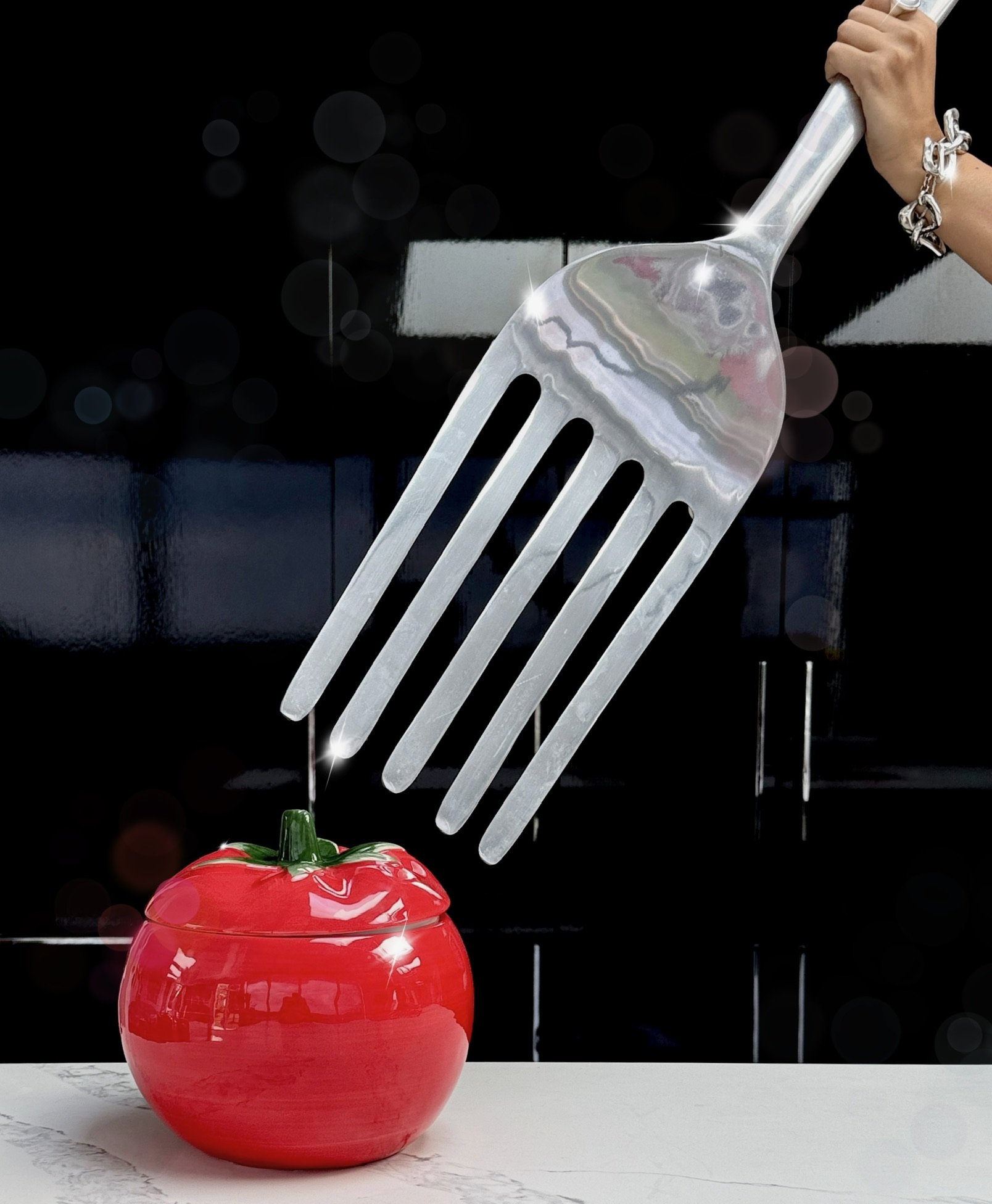 A hand with a large fork hovers over a red glass tomato.