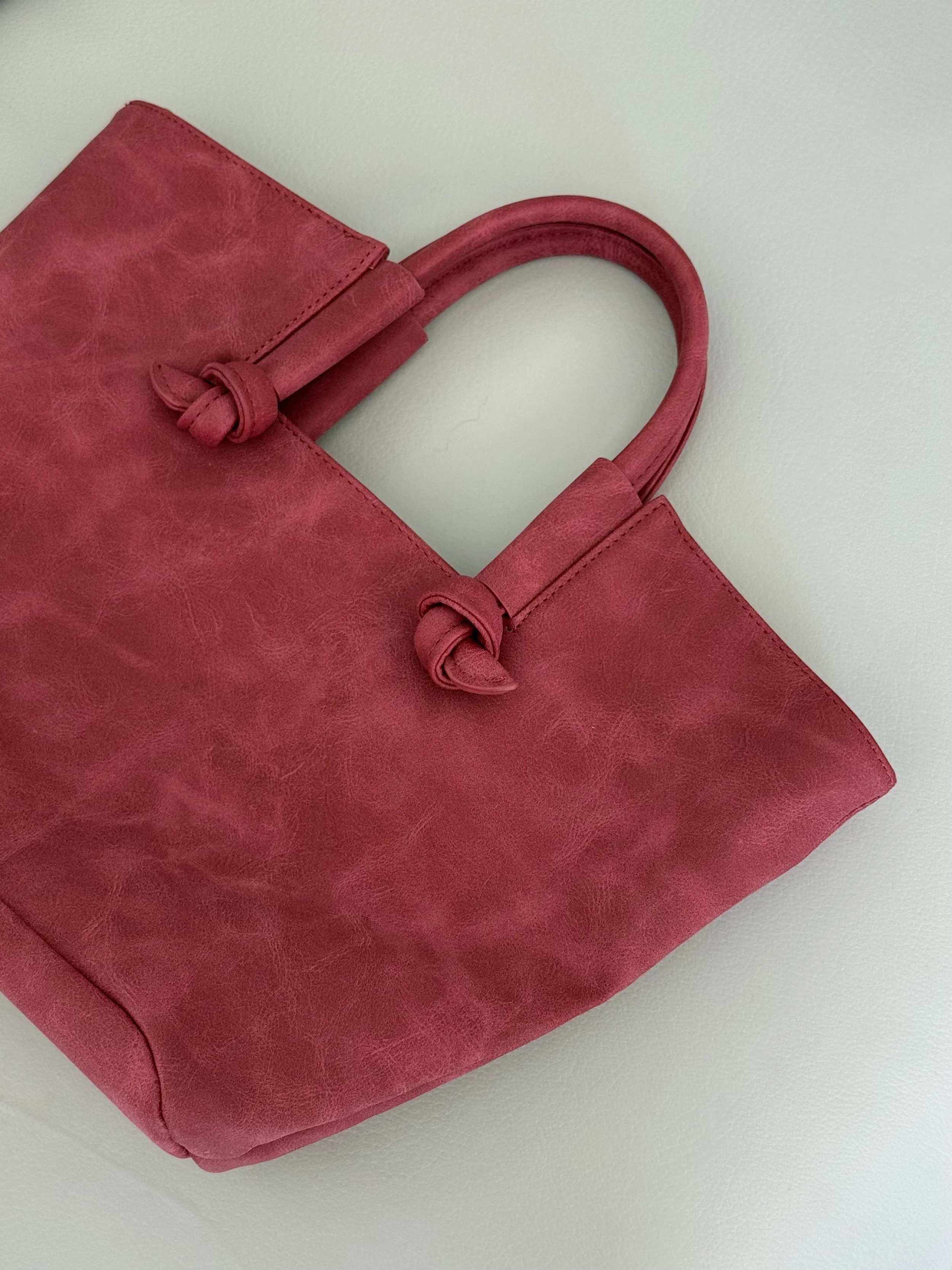 A pink leather handbag with knotted handles on a white surface.