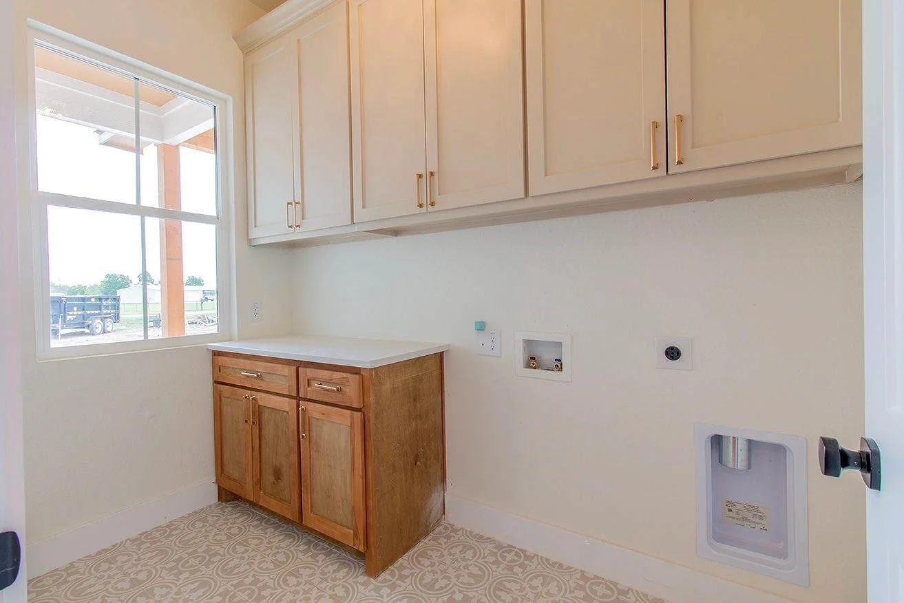 Empty laundry room with a large window, upper and lower cabinets, and hookups for washer and dryer.