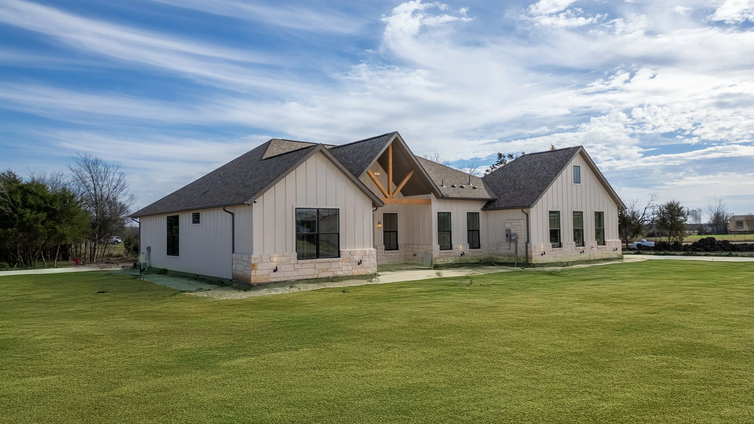 Large house under construction with metal siding and a pitched roof, surrounded by a green lawn and a partly cloudy sky.