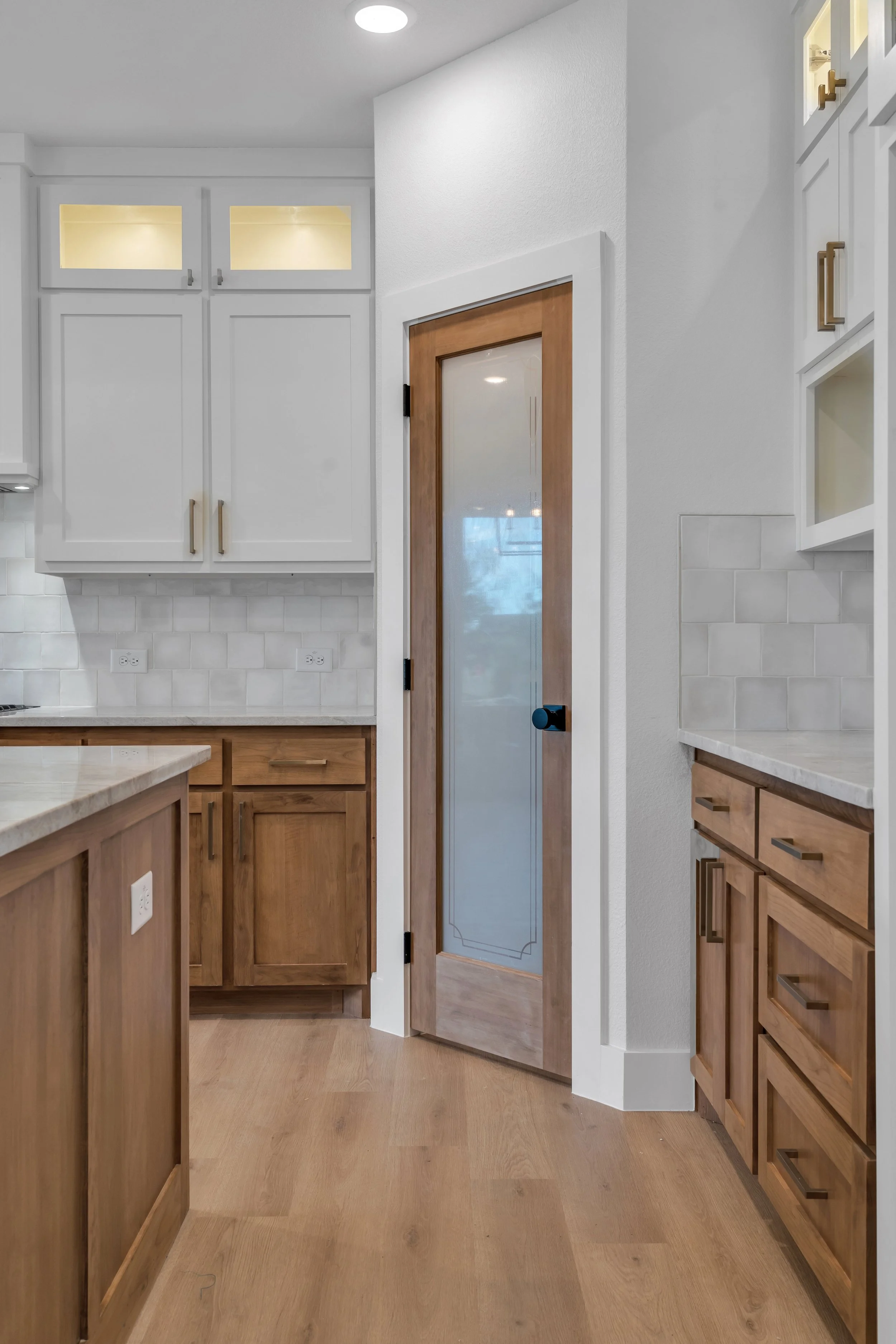 A view of a kitchen with wooden cabinets, a glass-paneled door, and white tiled backsplash.