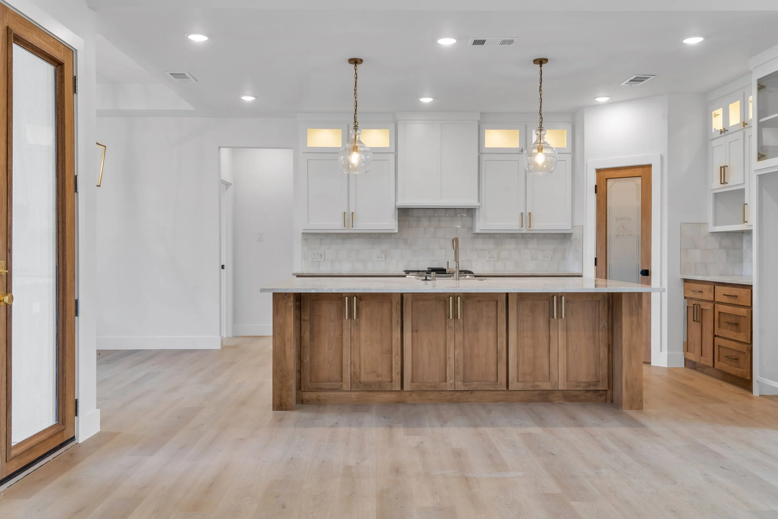 A modern kitchen with white cabinets, a wooden island, pendant lights, and light wood flooring.
