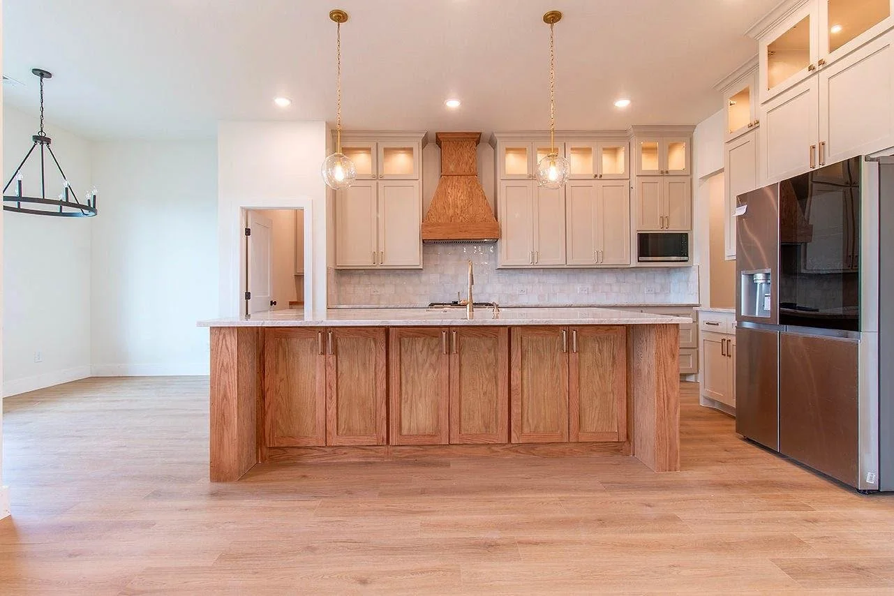 Modern kitchen with wooden island, white cabinetry, stainless steel refrigerator, and pendant lights.