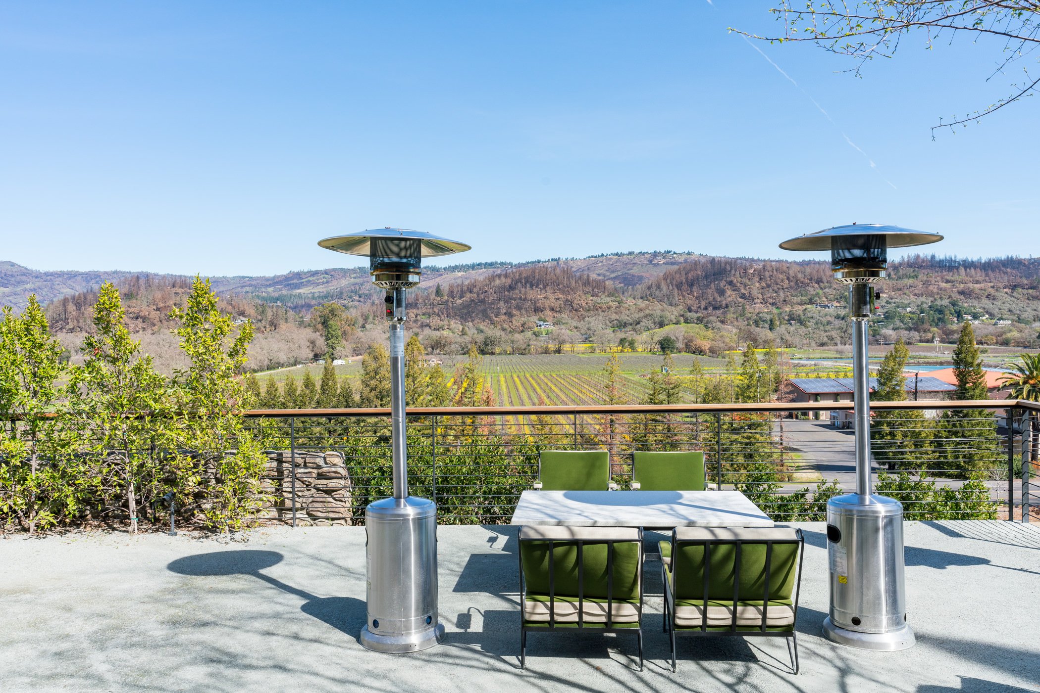 Outdoor patio with table, chairs, and heaters overlooking vineyard and hills