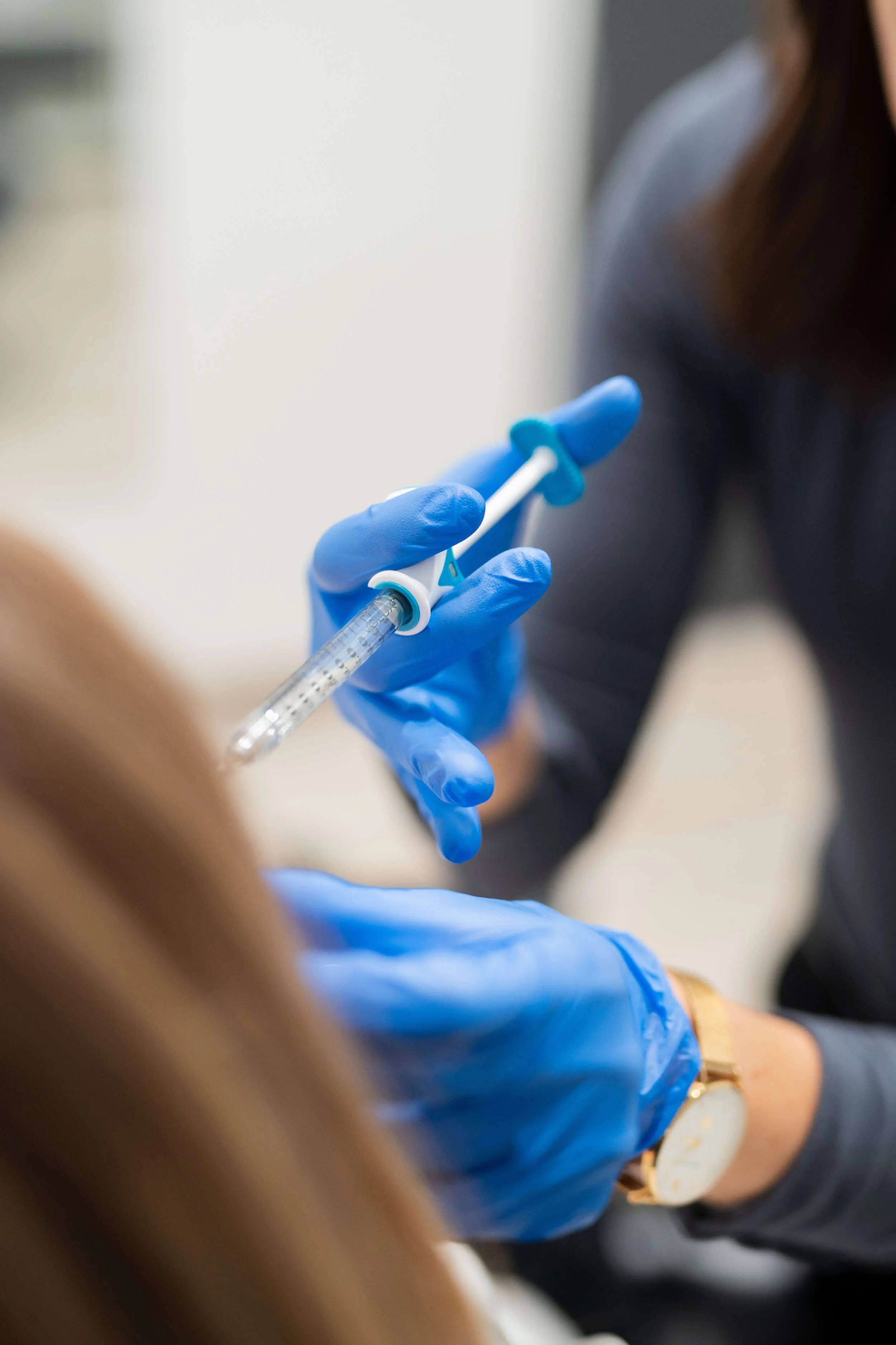 A healthcare worker wearing blue gloves holding a syringe, preparing to give an injection or vaccine to a patient.