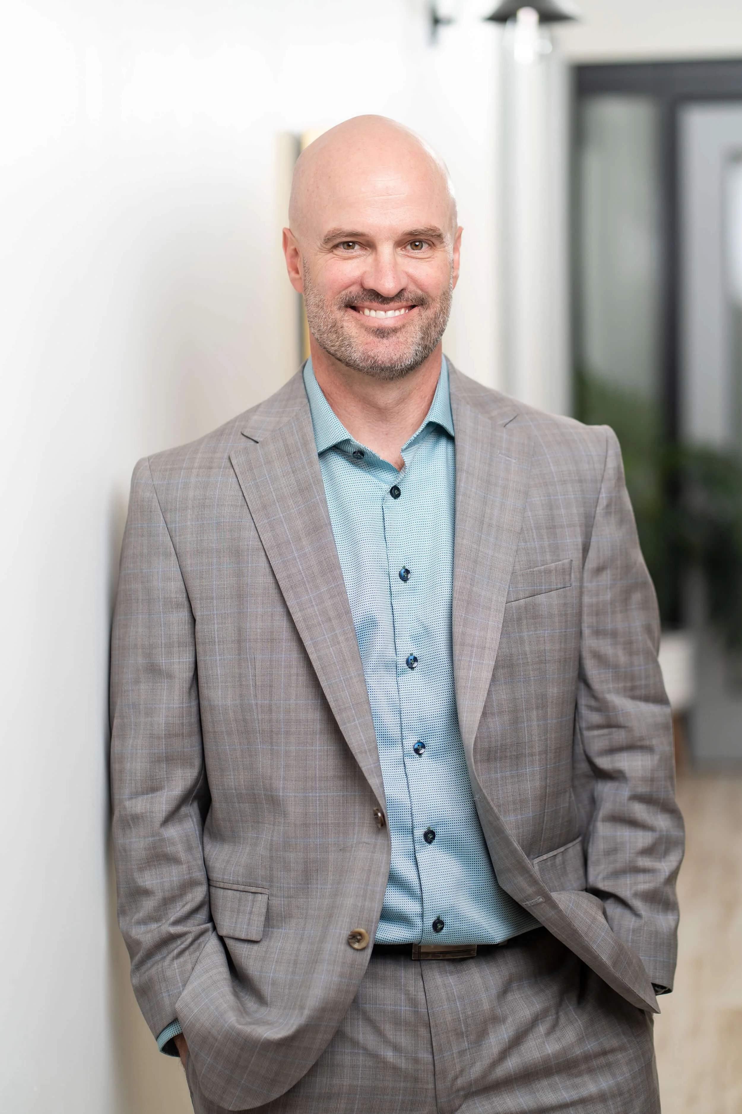 A man in a gray suit and light blue shirt, Dr. Chris Thomson, posing against a wall in his office.