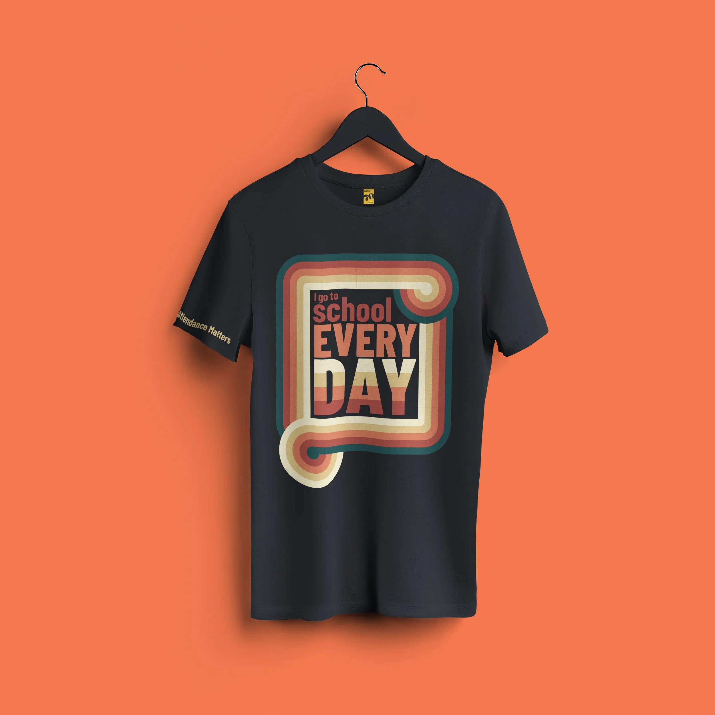 Black T-shirt hanging on a black hanger against an orange background. The shirt has a retro rainbow design with the text 'I go to school every day' on it.