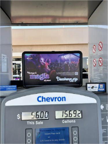 A Chevron gas pump displaying a sale of $56.00 for 15.692 gallons of fuel, with a promotional sign for vaccines and a digital screen on top showing a nighttime concert scene.