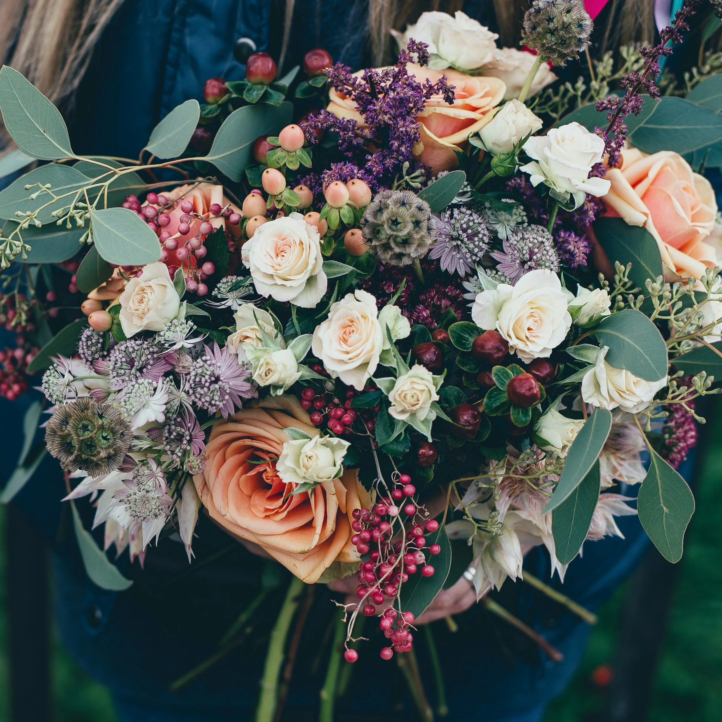 A person's hands holding a large bouquet of mixed flowers including roses, berries, and greenery.