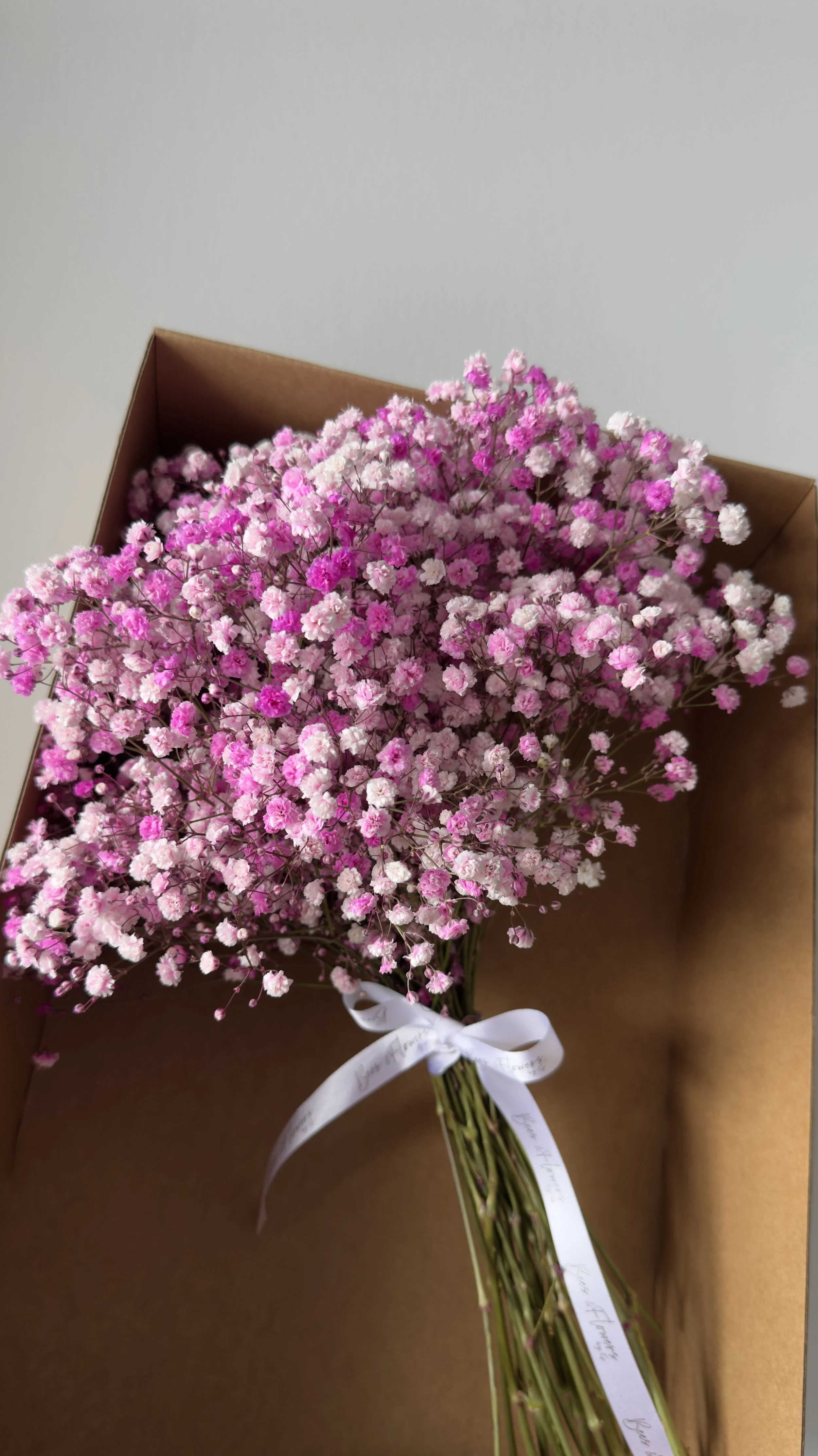 A bouquet of pink and white Gypsophila flowers tied with a white ribbon and placed in a cardboard box.