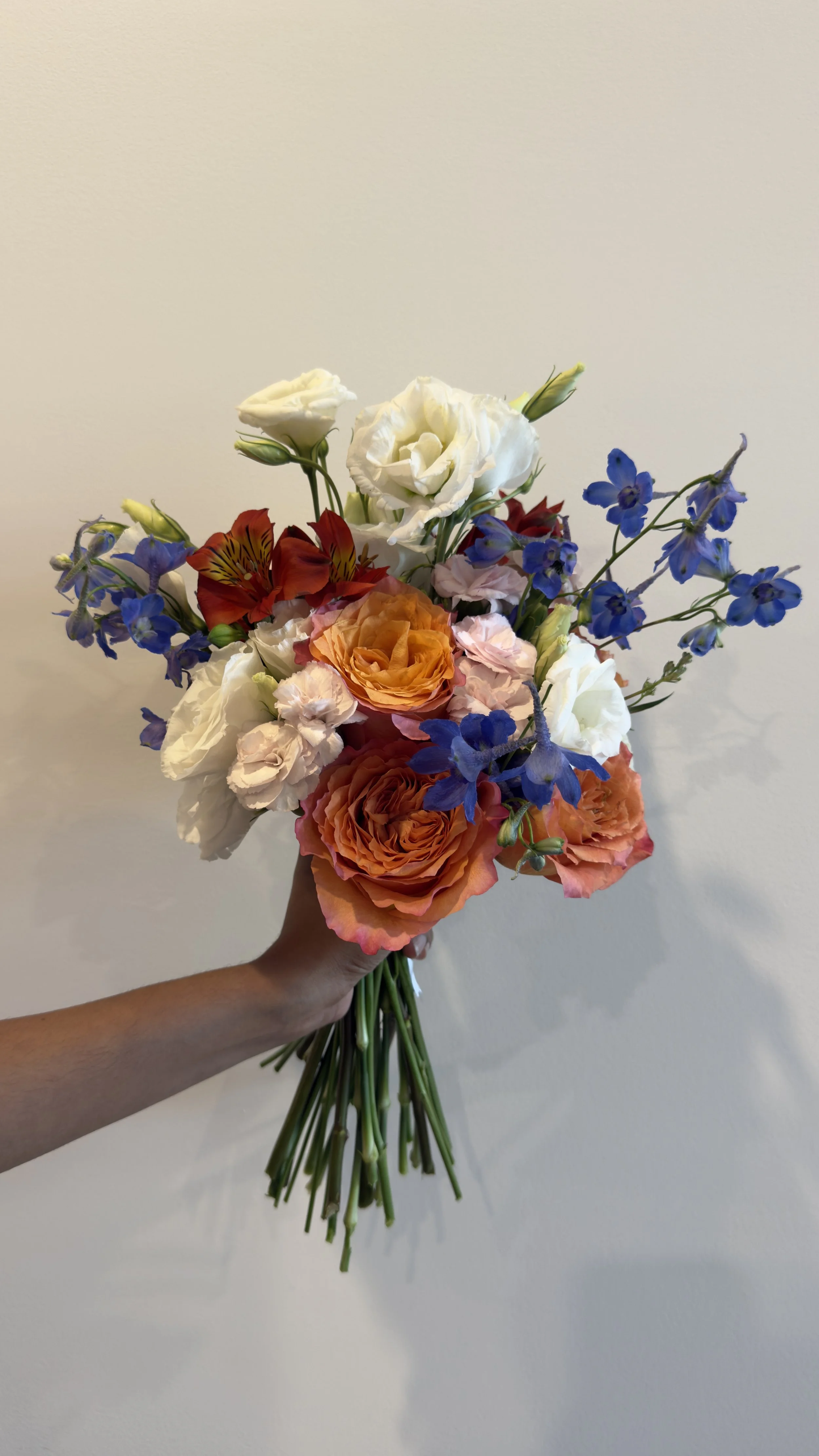 A hand holding a bouquet of colorful flowers against a plain white background.