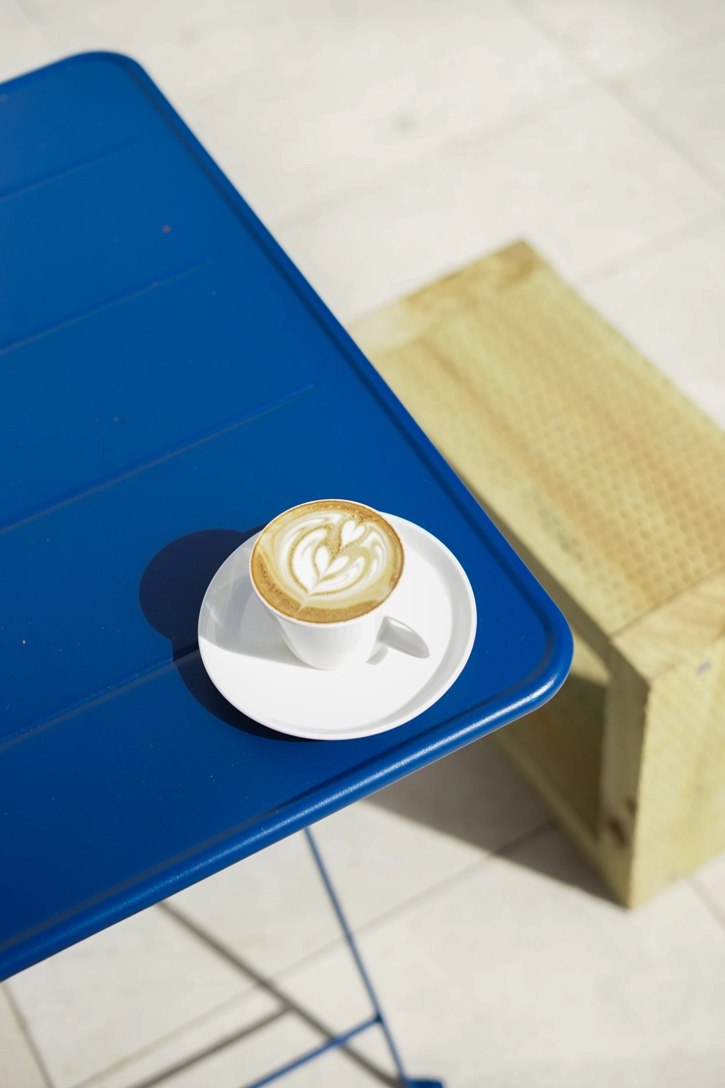 A cup of coffee with latte art on a white saucer, placed on a blue table.