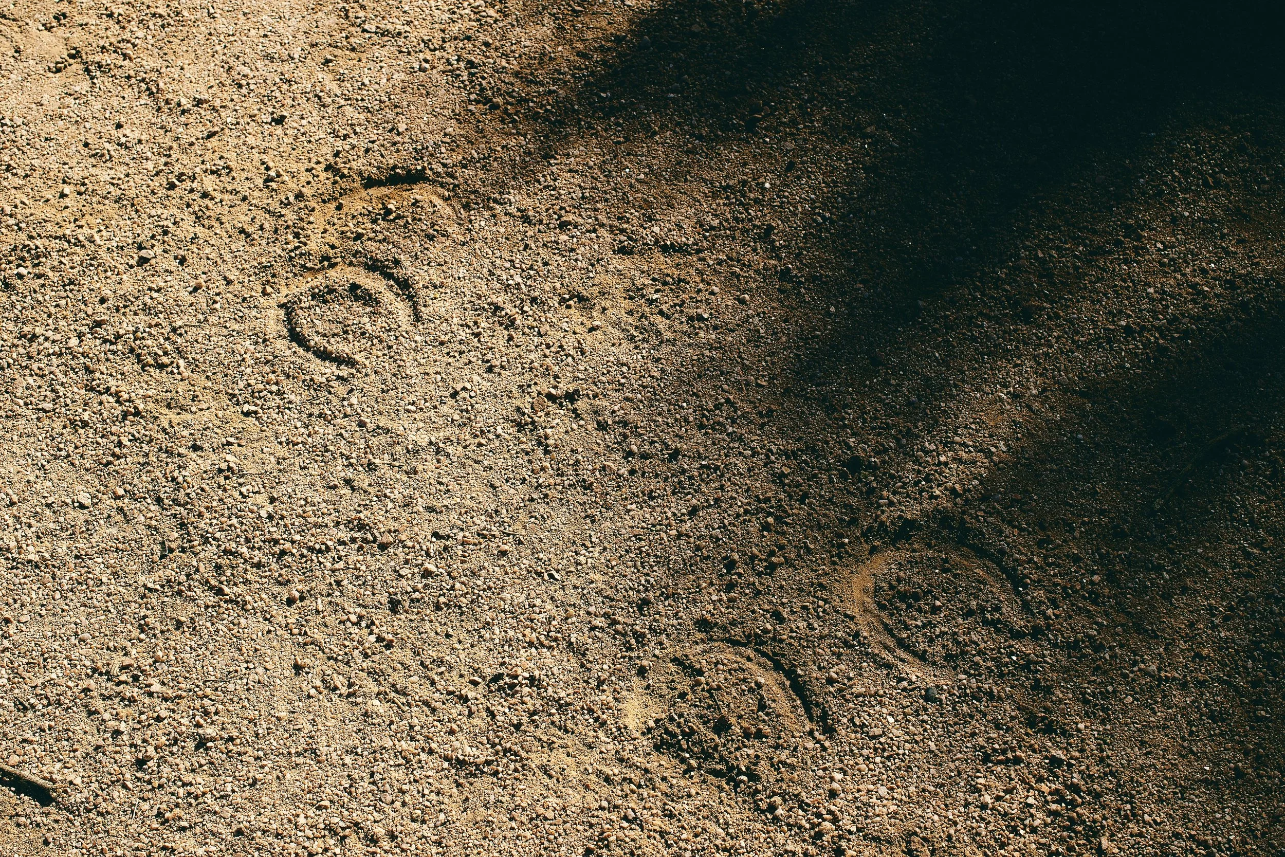 Close-up view of sandy ground with small pebbles, showing the marks of a bicycle tire.
