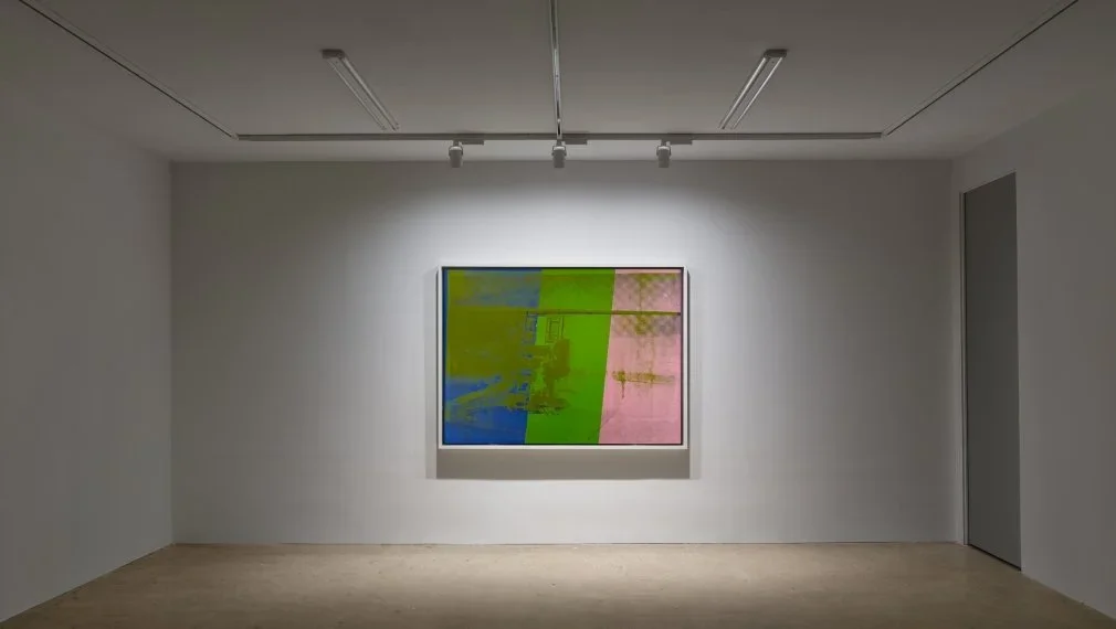 Abstract artwork with divided sections in blue, green, and pink hanging on a white gallery wall.