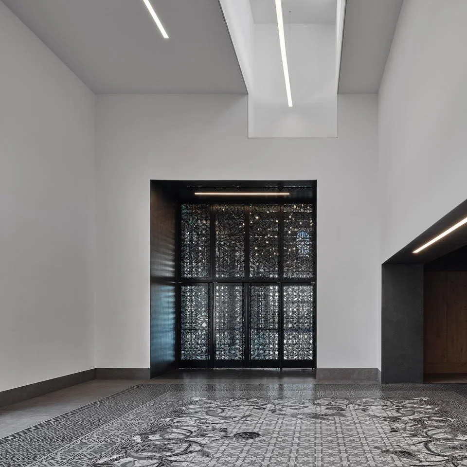 Modern interior space with white walls, a patterned black and white floor, and a decorative black window with intricate design. Ceiling features recessed lighting.