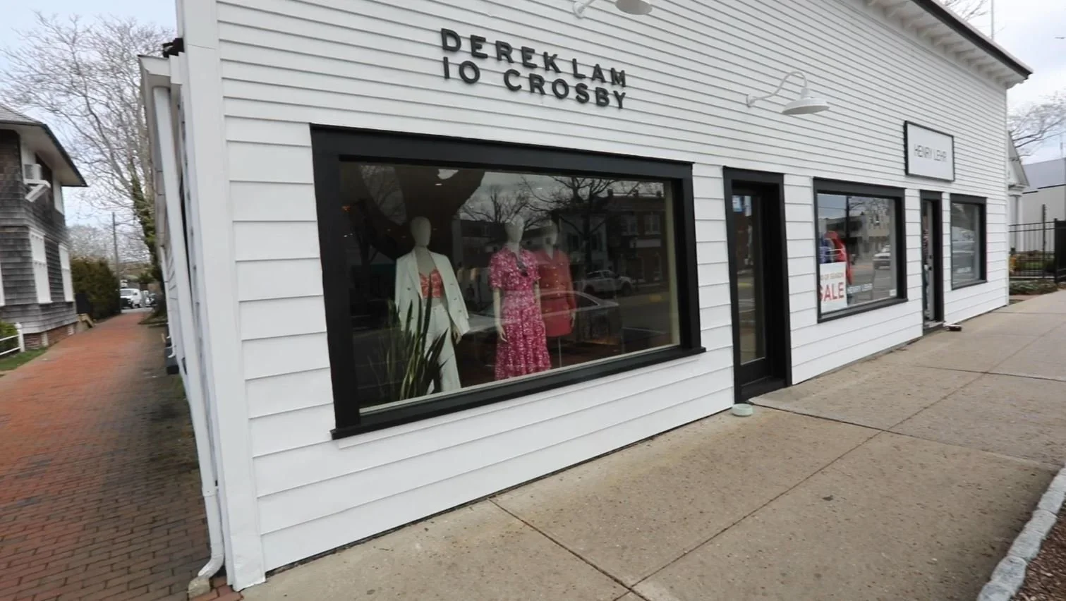 White storefront with black window frames, mannequins in a display window wearing dresses, and signage that reads "Dereklam to Crosby" on the building's exterior.