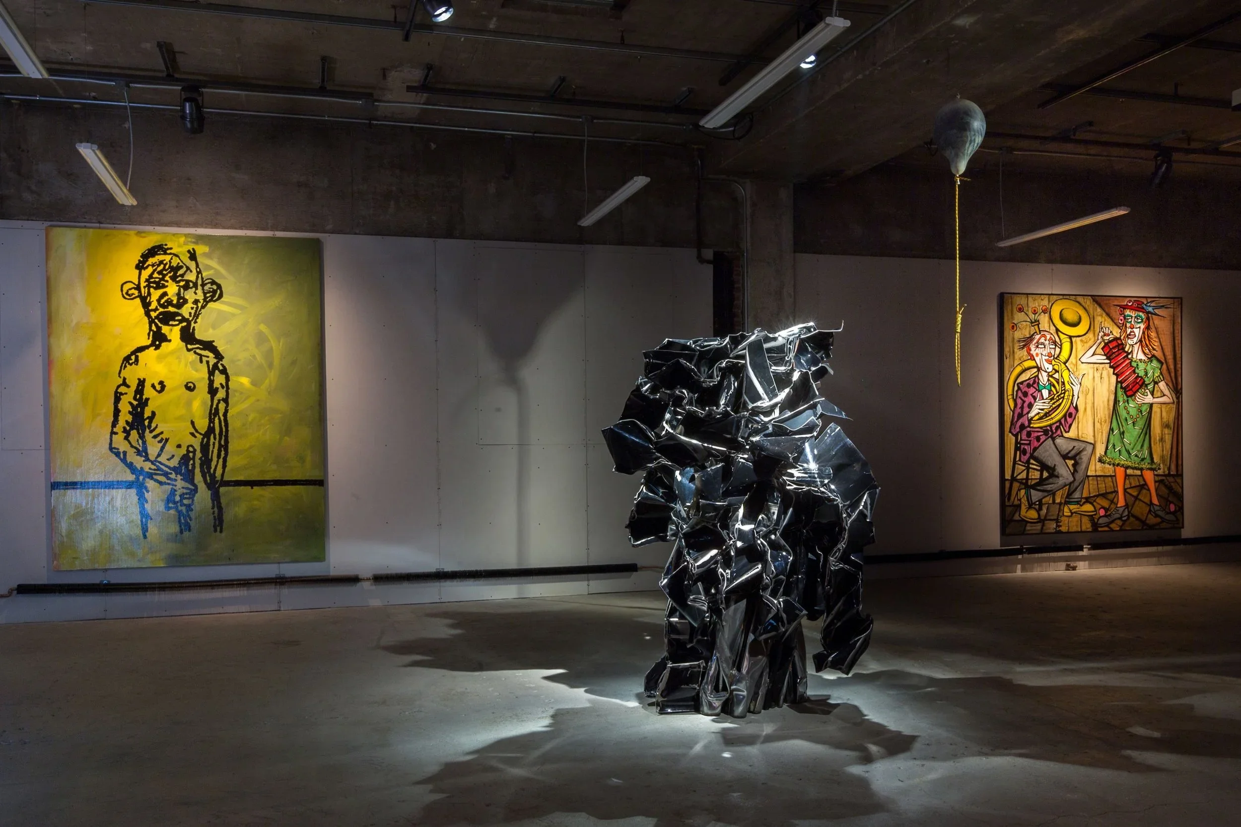 Metal abstract sculpture in a gallery with graffiti-style paintings on the walls.