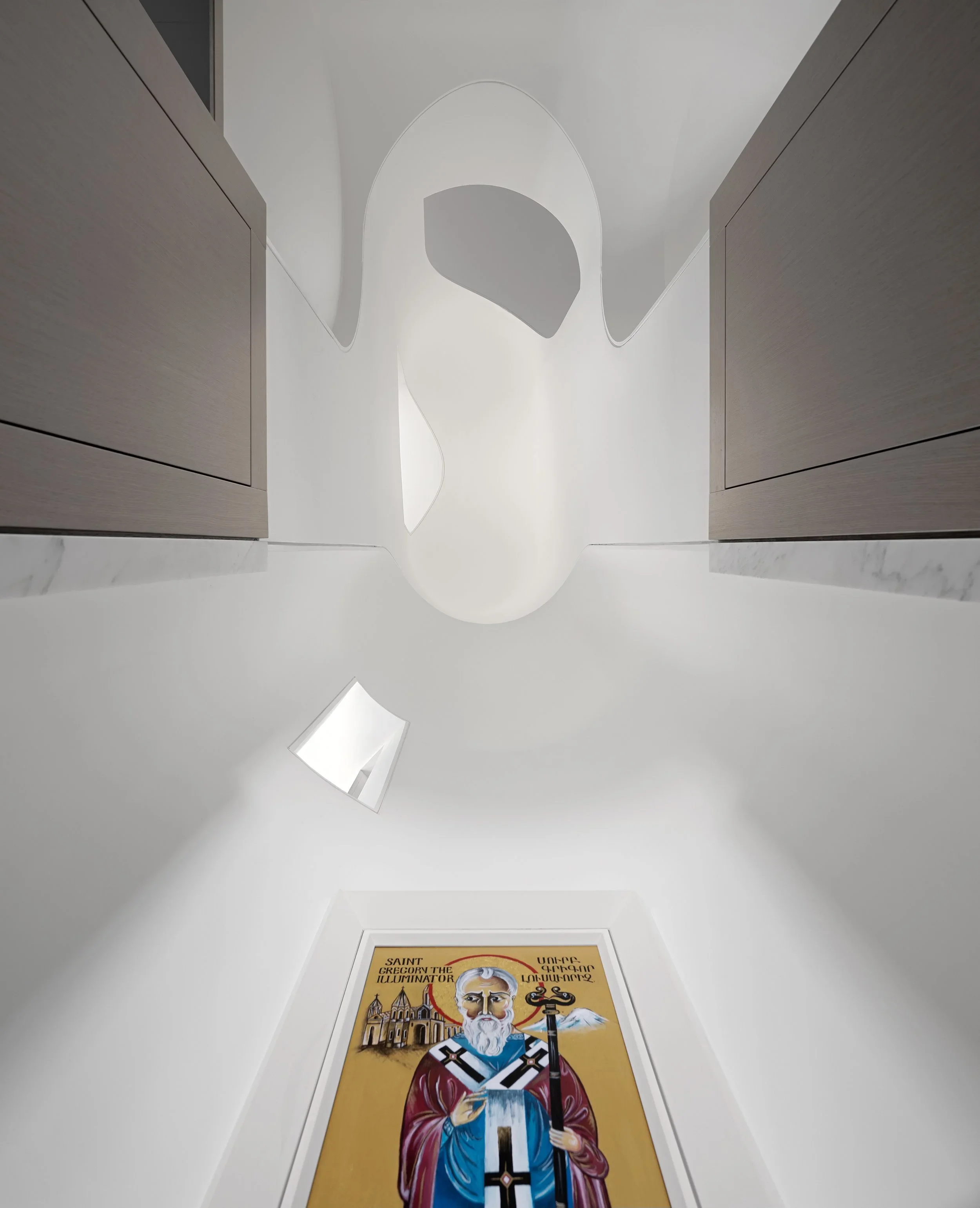 Looking up at a white gallery ceiling with abstract shapes, a wall-mounted light, and a religious icon painting of Saint Gregory the Illuminator with Armenian script.