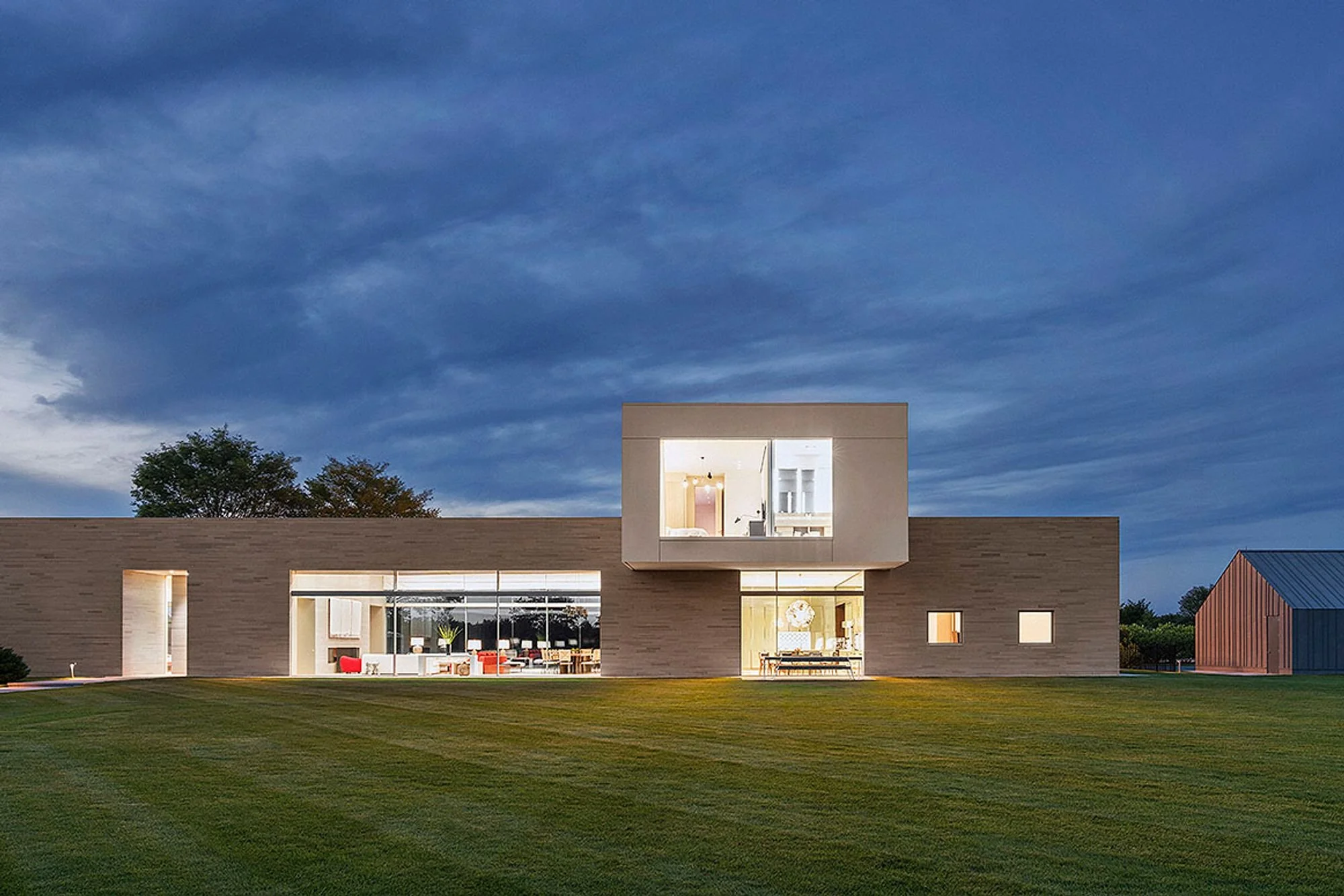 Modern house with large windows, a rectangular design, and a grassy lawn at dusk