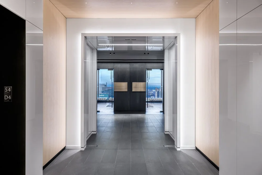 Modern office building corridor leading to glass doors with a city view outside.