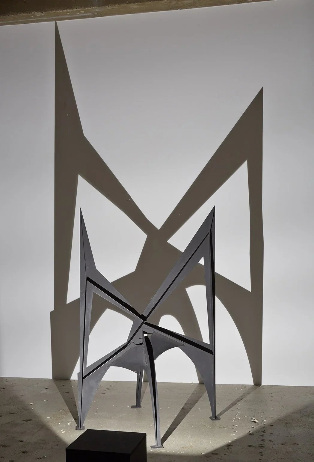 Abstract modern sculpture made of metal with geometric shapes, casting shadows on a plain wall.