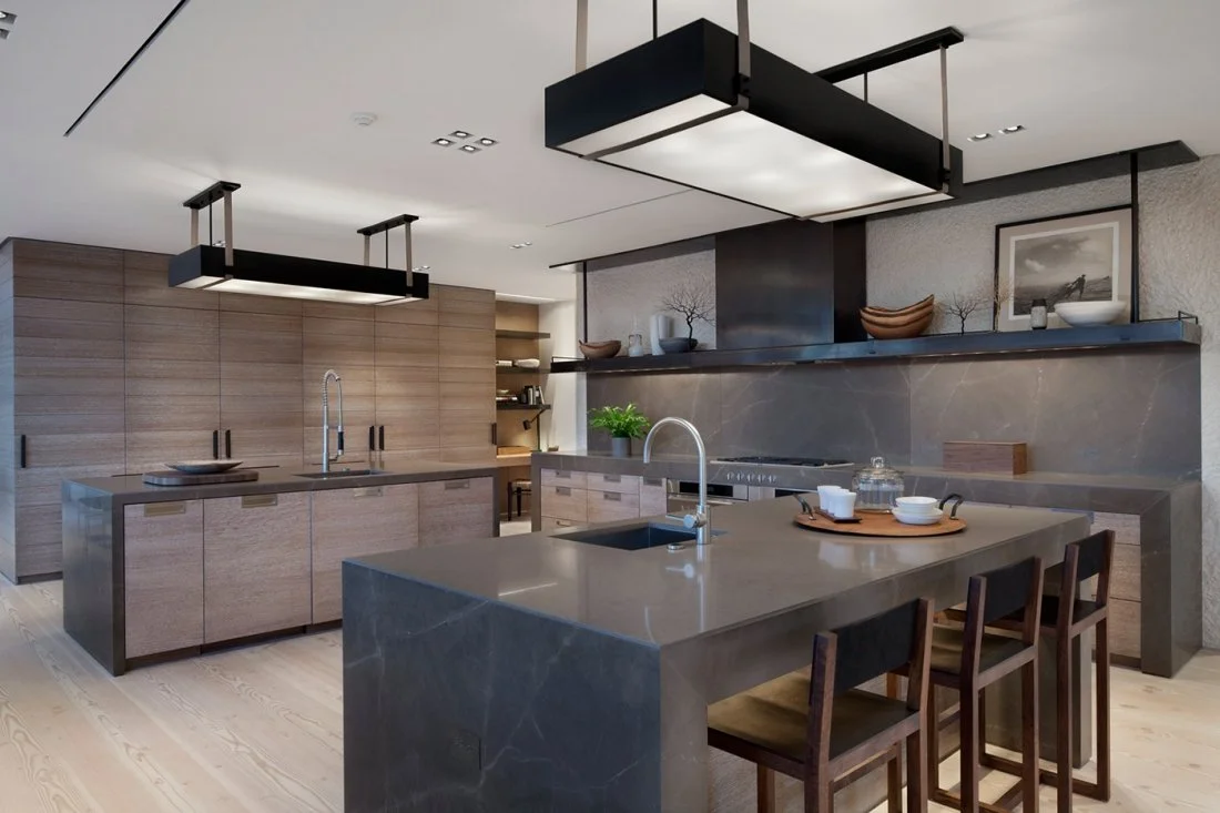 Modern kitchen with light wood cabinets, marble island with pink cherry blossom arrangement, and granite countertops, illuminated by a large rectangular ceiling light.