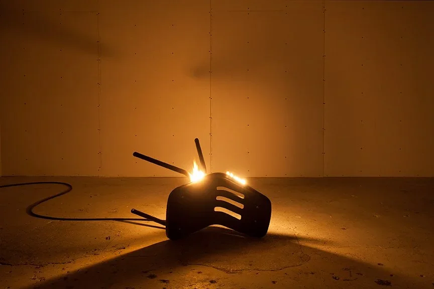 A black hairdryer on the floor with flames coming out of the vents, casting a shadow on the wall.