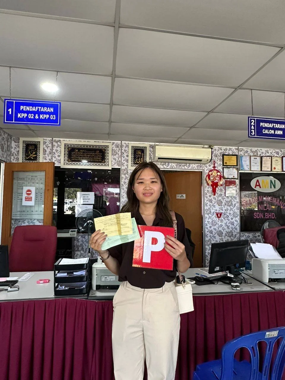 A young woman holding a passport and documents inside a registration office with signs, desks, and office equipment.