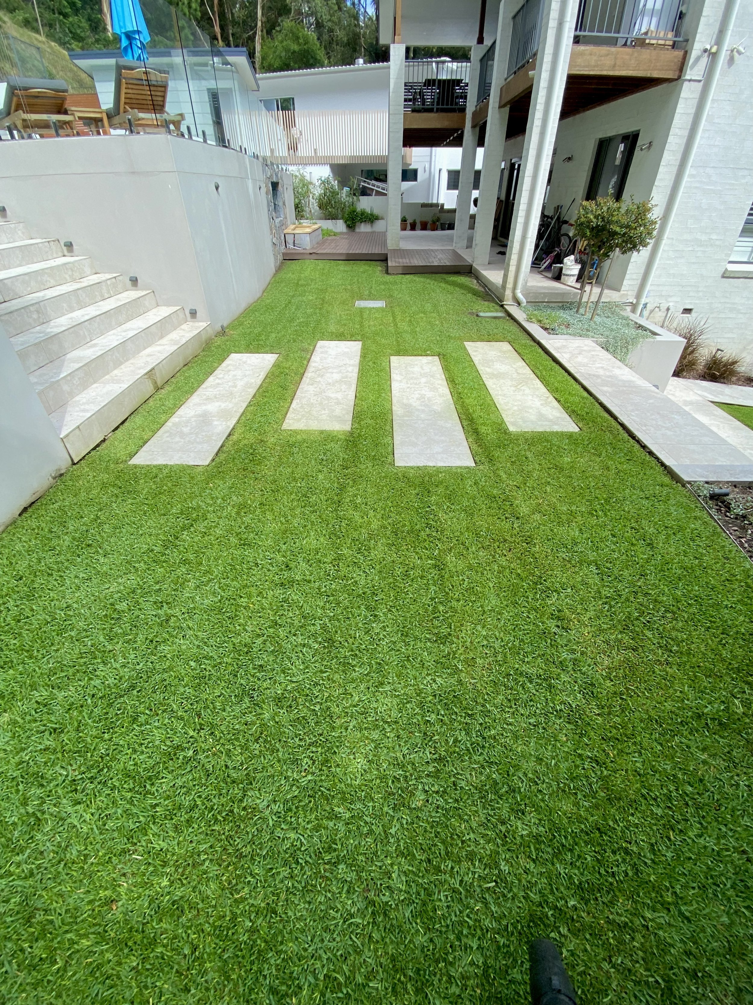 Modern backyard with green lawn, stone walkway, stairs, and patio seating